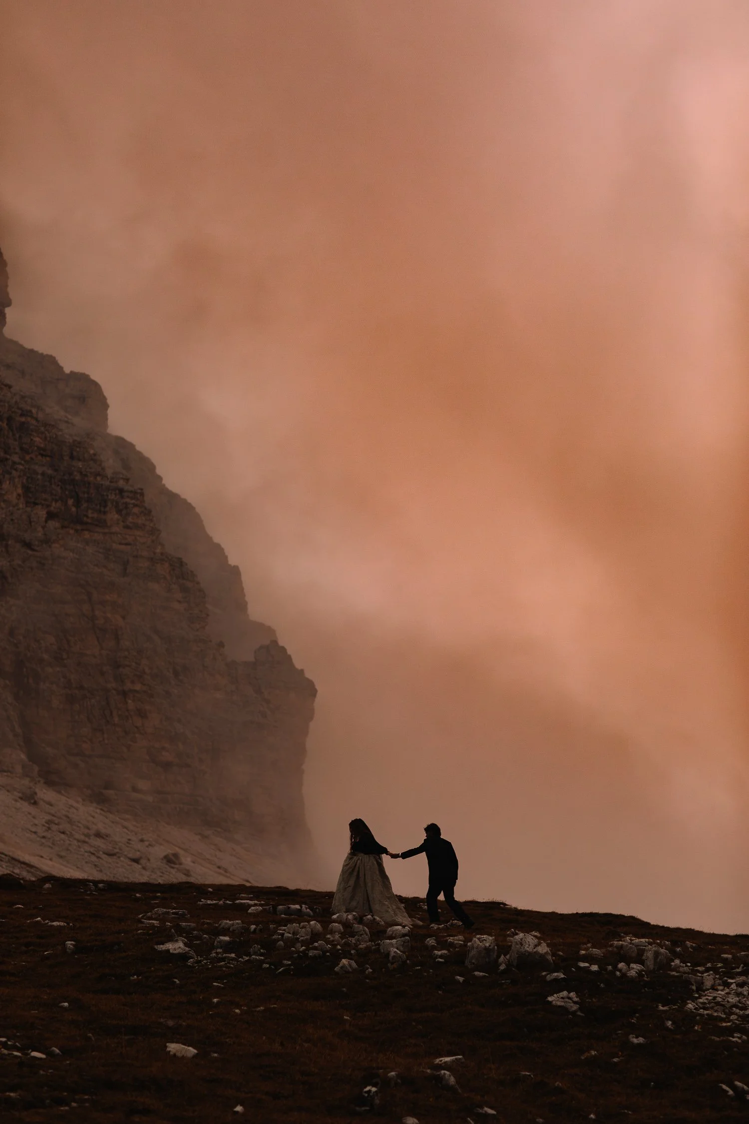 Couple holding hands while walking across a dramatic mountain landscape during an adventure elopement
