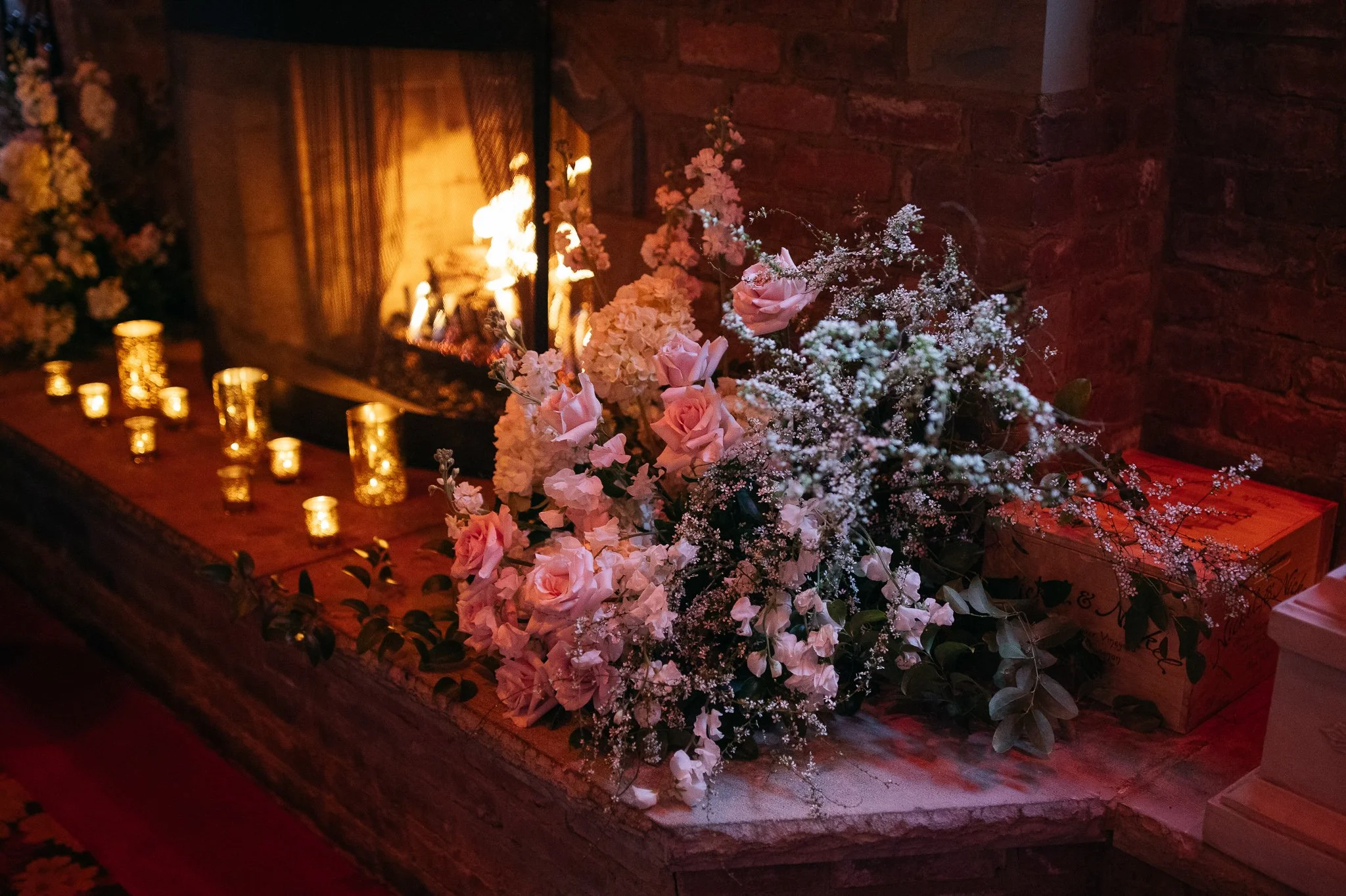 Floral arrangement and candles set along fireplace during wedding dinner