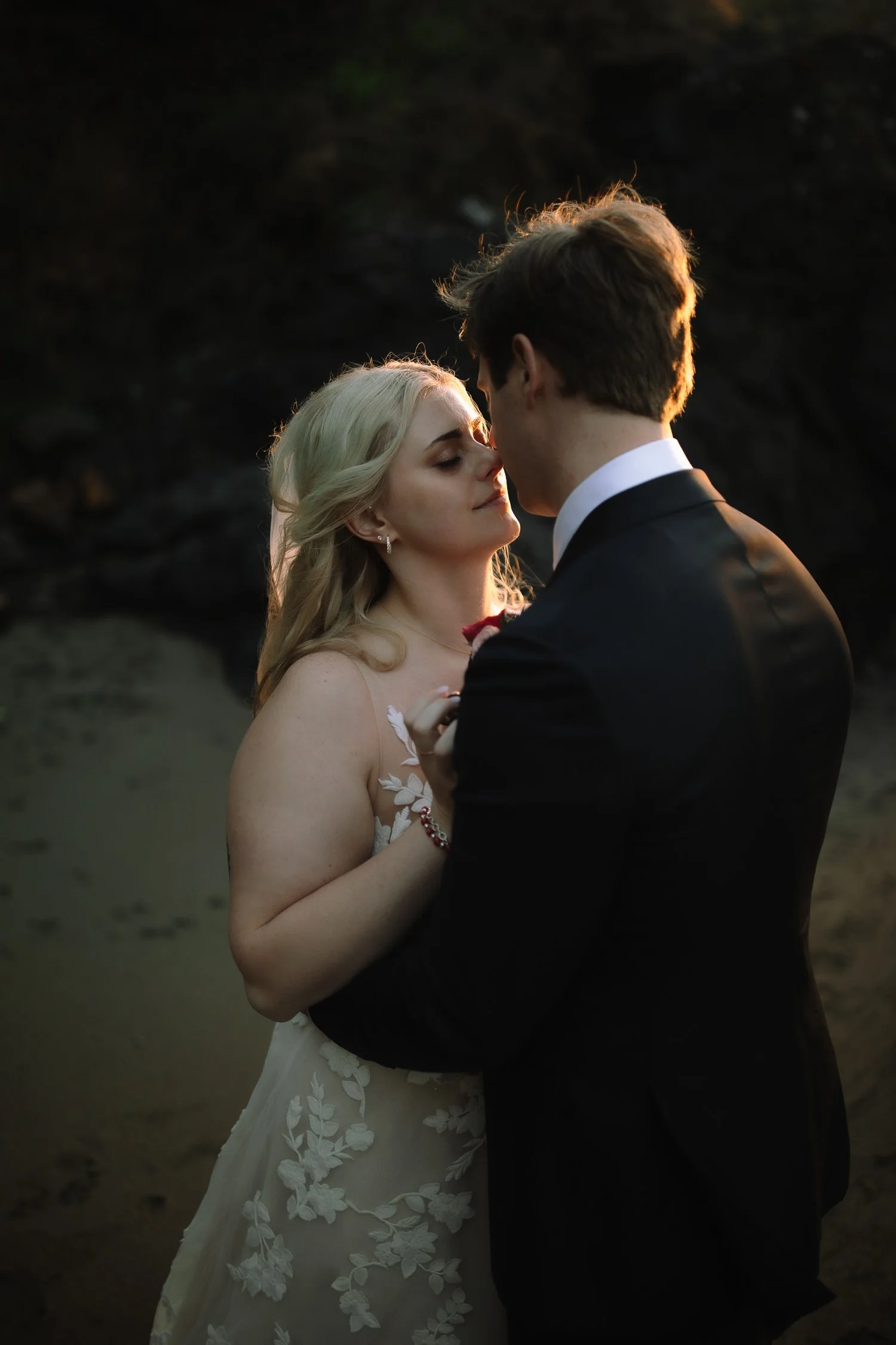 Bride and groom embracing near dark rock formations at sunset