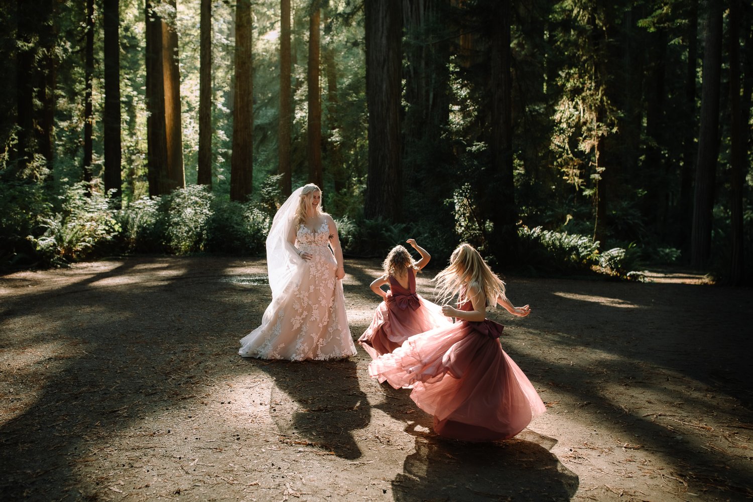 Flower girls twirling in sunlit forest clearing during redwoods wedding