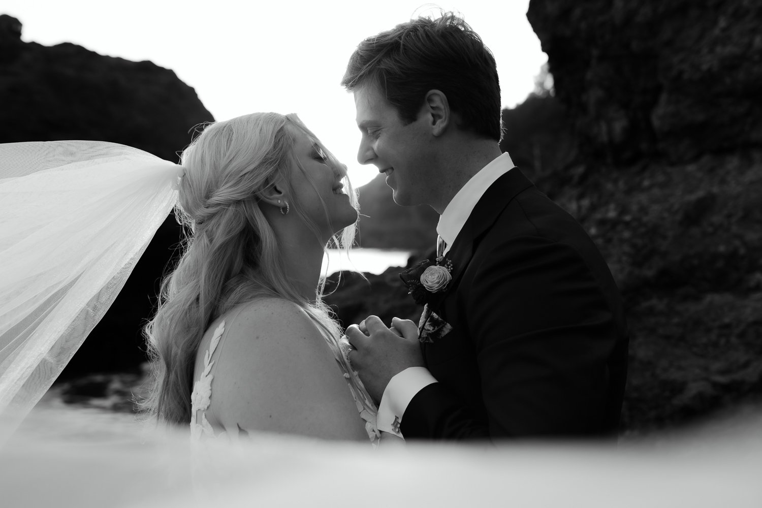 Black and white close-up of bride and groom smiling together on the coast