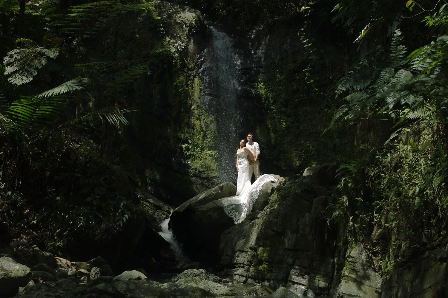 Bride and groom standing beneath a waterfall in El Yunque National Forest during an intimate rainforest elopement in Puerto Rico.