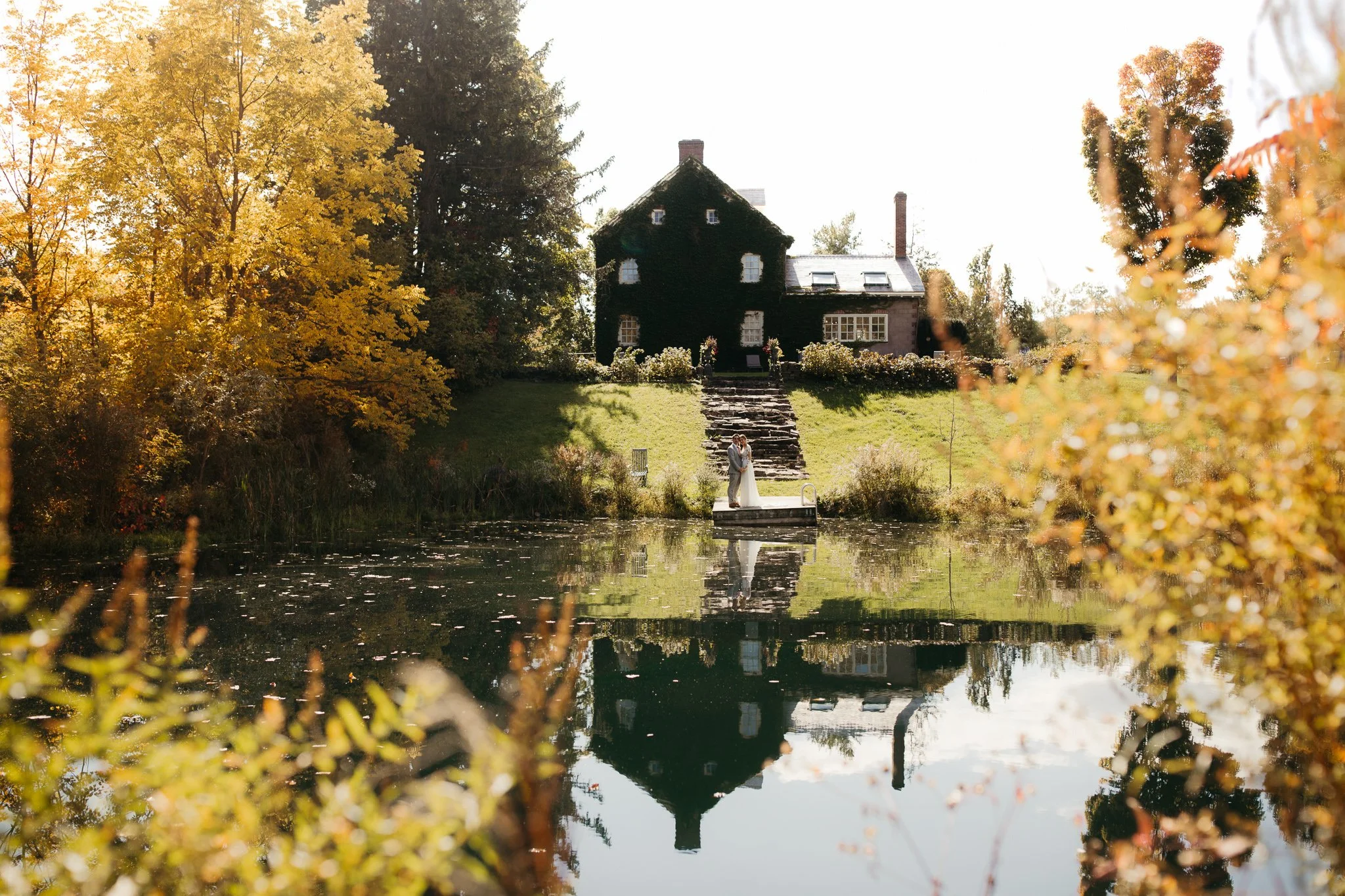 Couple standing on the dock at Windrift Hall in the Hudson Valley surrounded by early autumn trees