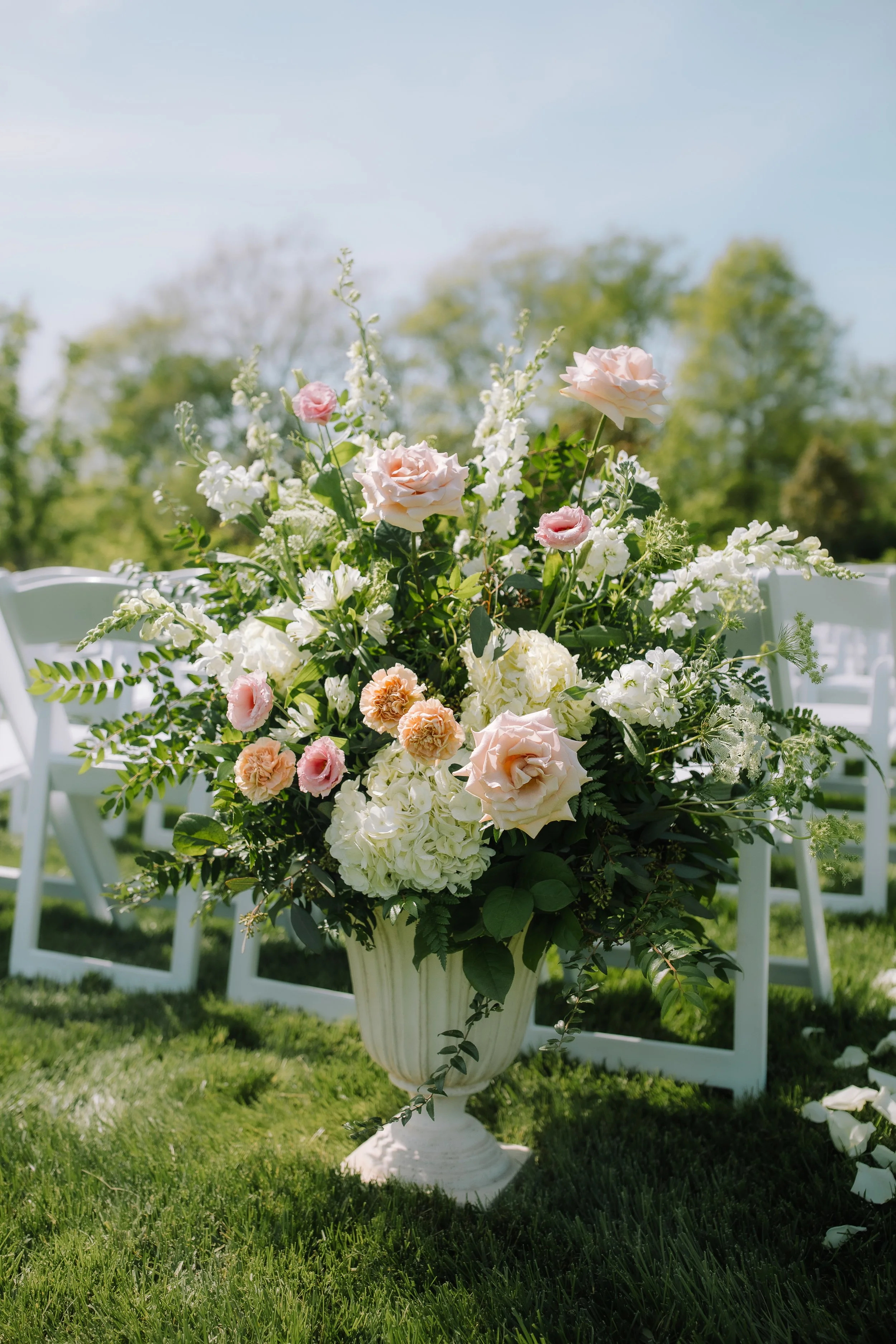 Large spring floral arrangement beside white ceremony chairs on the lawn at Jorgensen Farm The Gardens.