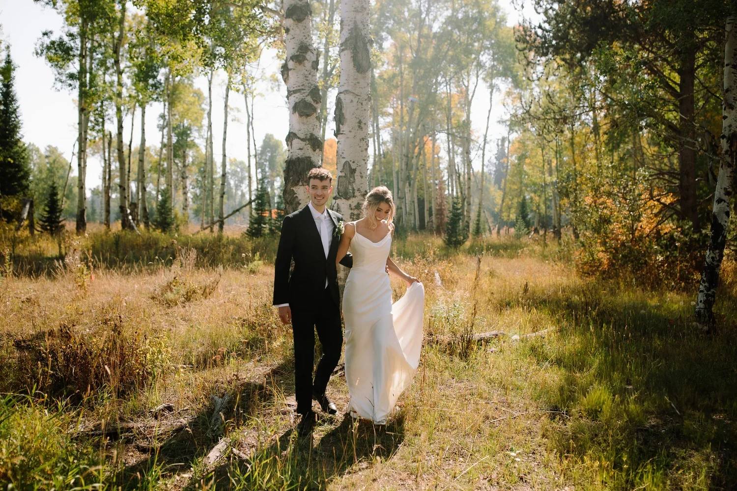Bride and groom walking through a sunlit aspen grove during their Jackson Hole wedding portraits