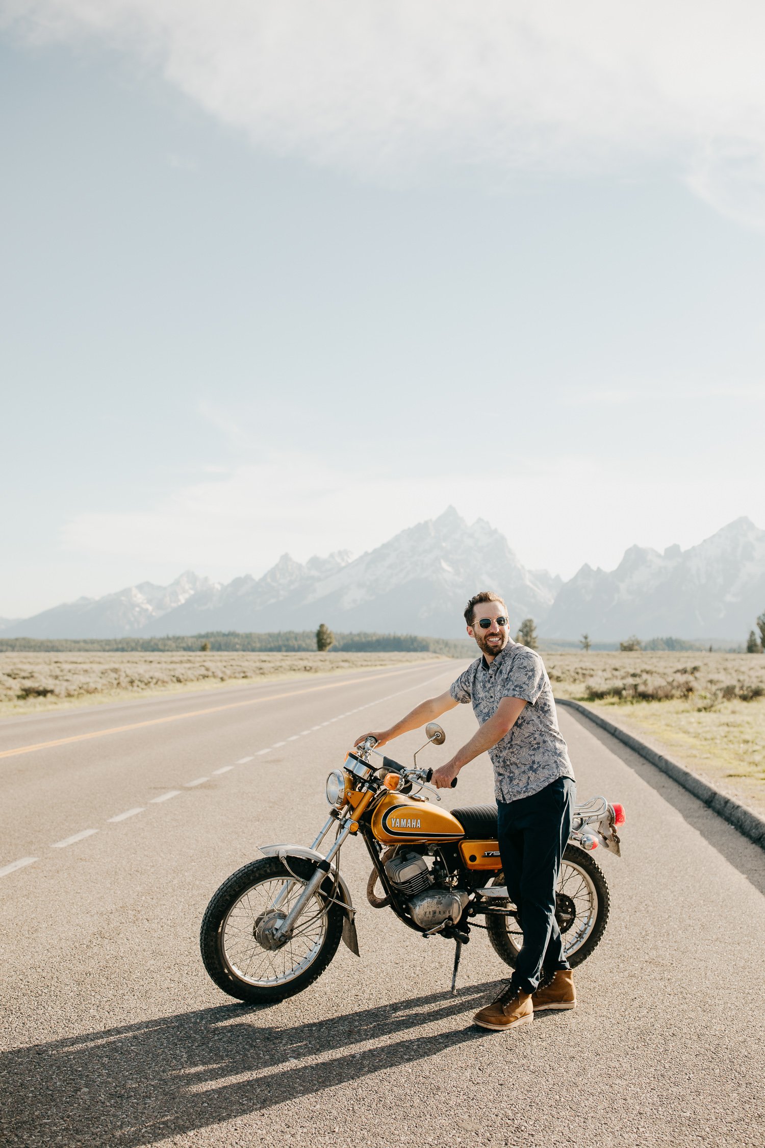 Man pushing vintage motorcycle during engagement session in Jackson Hole Wyoming