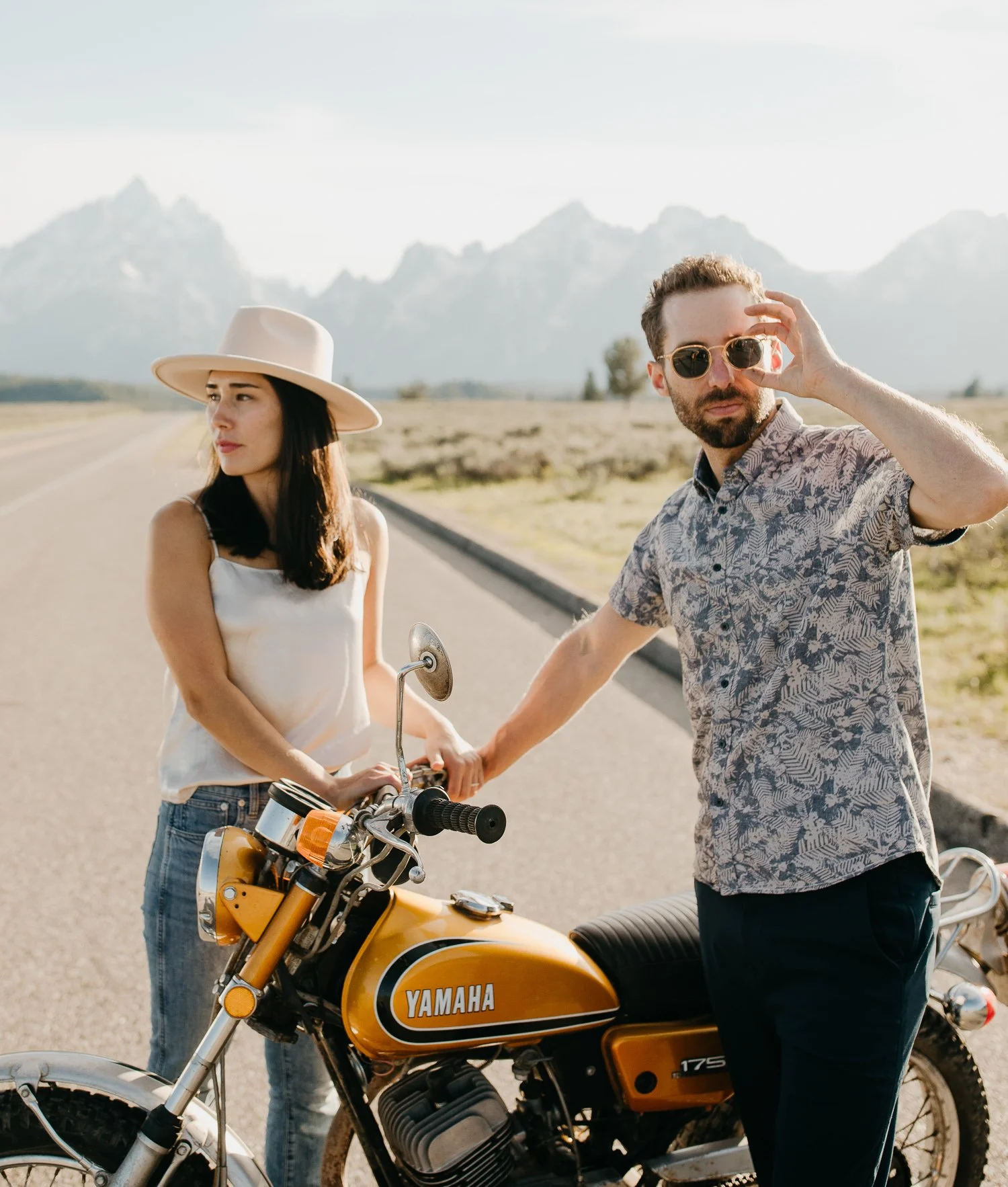 Engaged couple standing close beside a motorcycle during an outdoor engagement session
