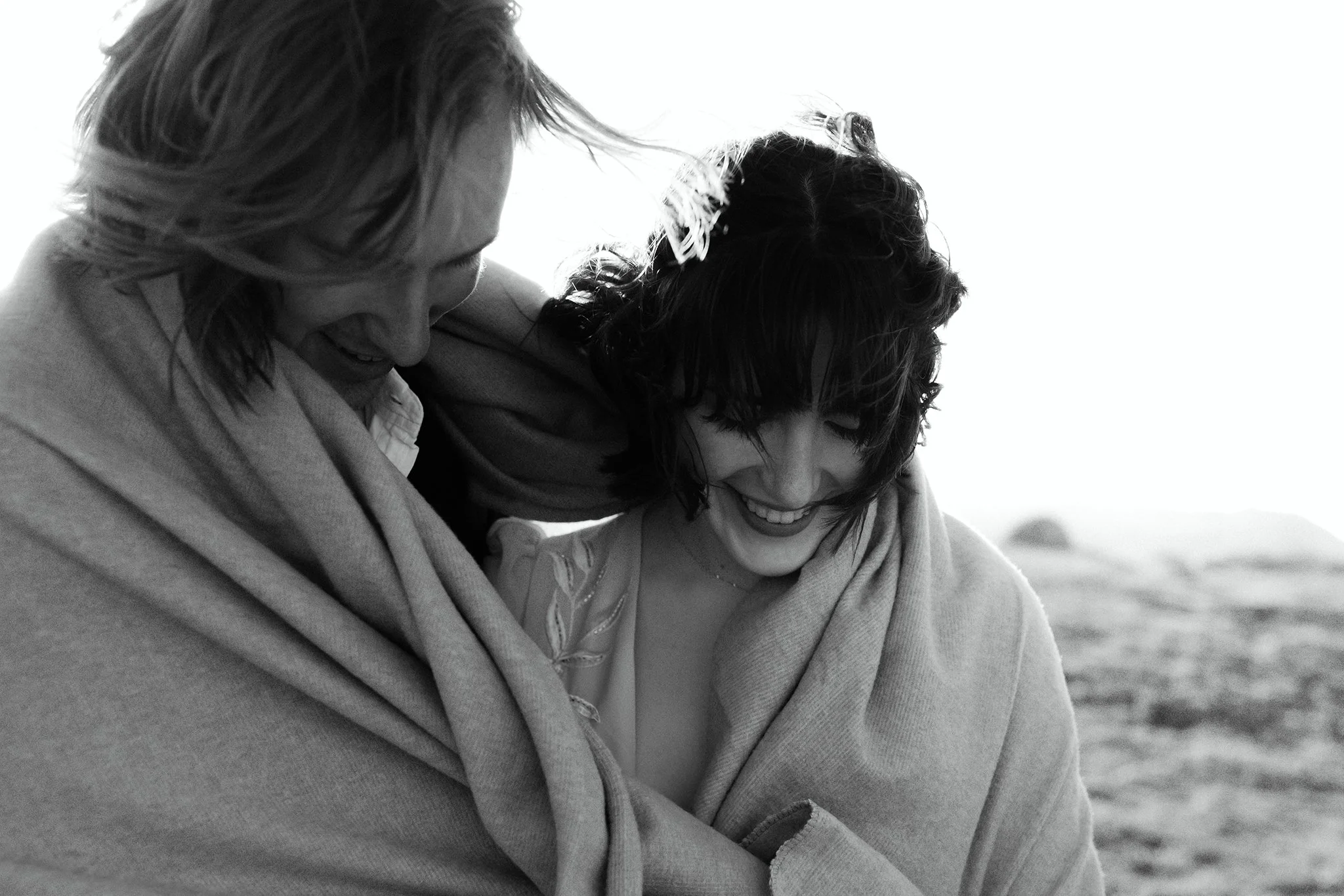 Couple wrapped in a blanket sharing a quiet, candid moment together outdoors