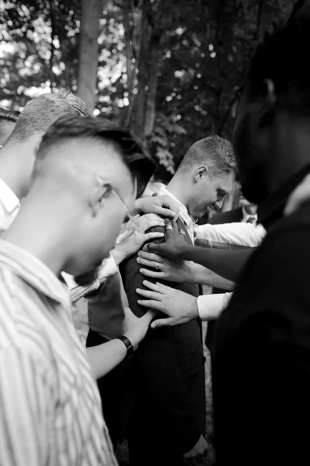 Candid wedding photo of friends praying over groom before ceremony, emotional wedding moment