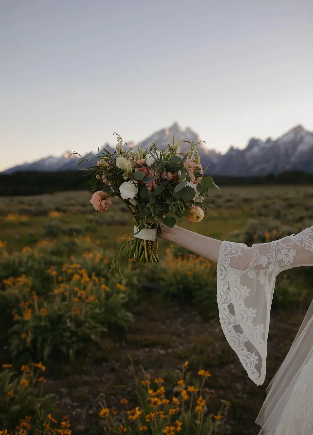 Bride holding a bouquet of wildflowers with the Tetons softly blurred in the background