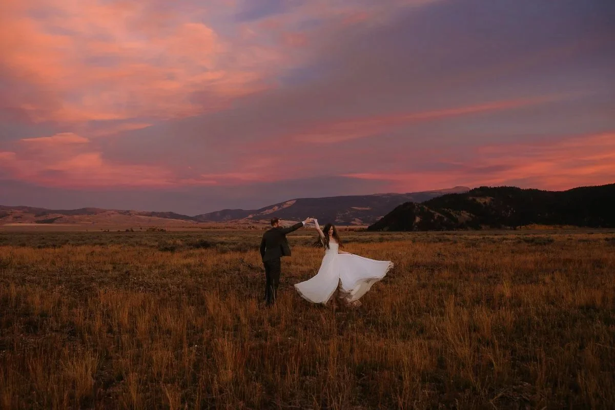 Couple dancing together in an open field at sunset with warm tones across the landscape