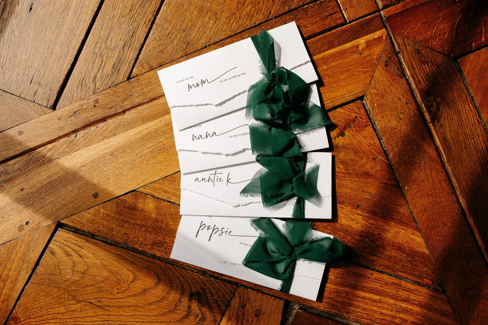 Wedding escort cards with green ribbon bows arranged on wood floor
