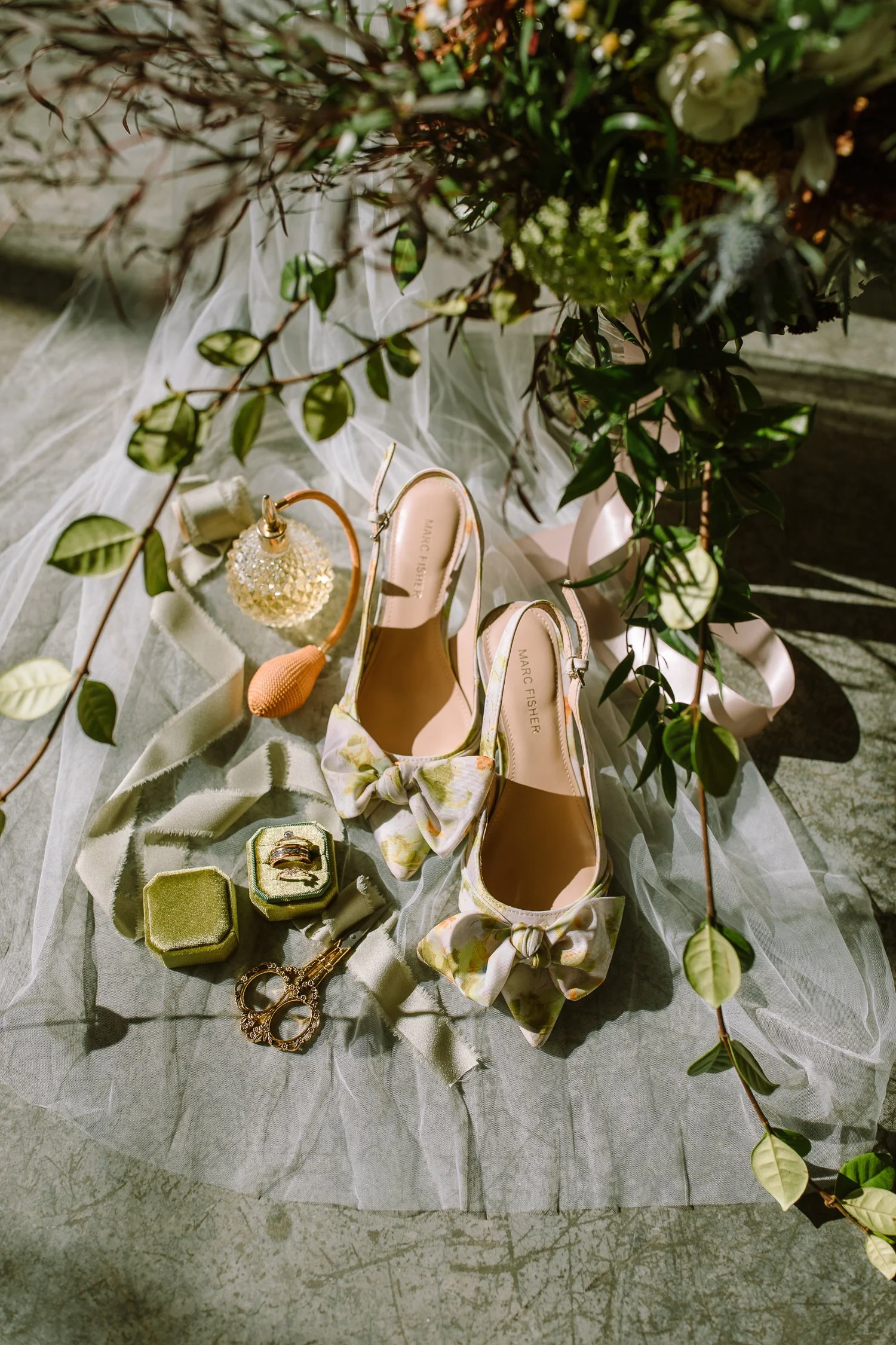 Bridal detail flat lay at Ivory Meadows wedding in Yellow Springs, Ohio featuring wedding rings, floral bridal shoes, perfume bottle, and greenery styled in natural light.