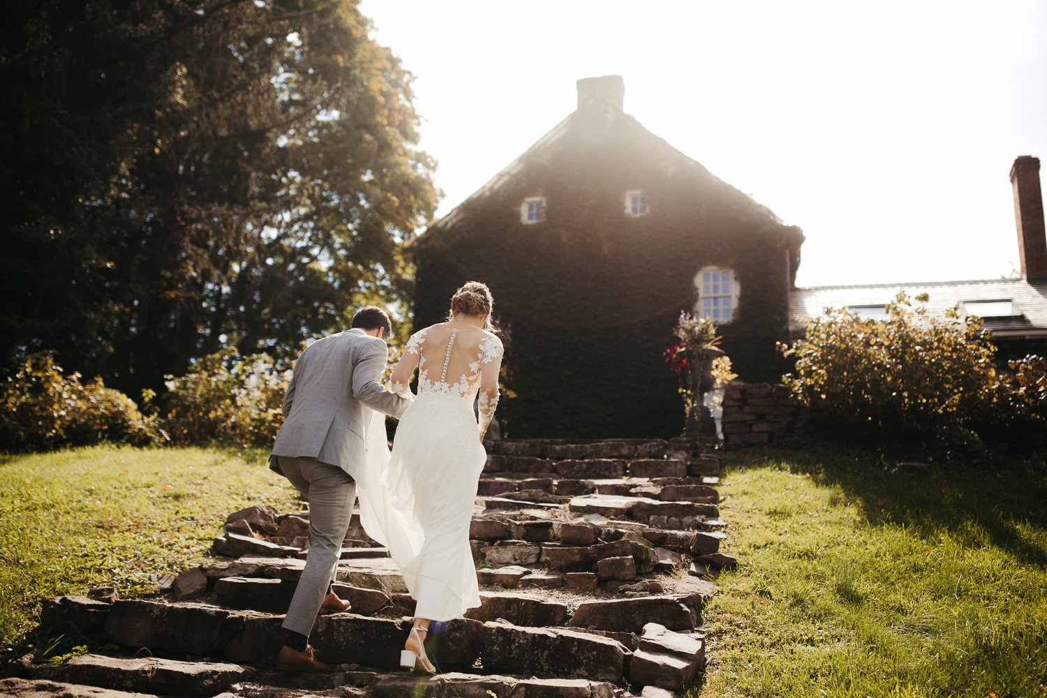Bride and groom walking up the stone steps toward the ivy covered Windrift Hall estate in the Hudson Valley