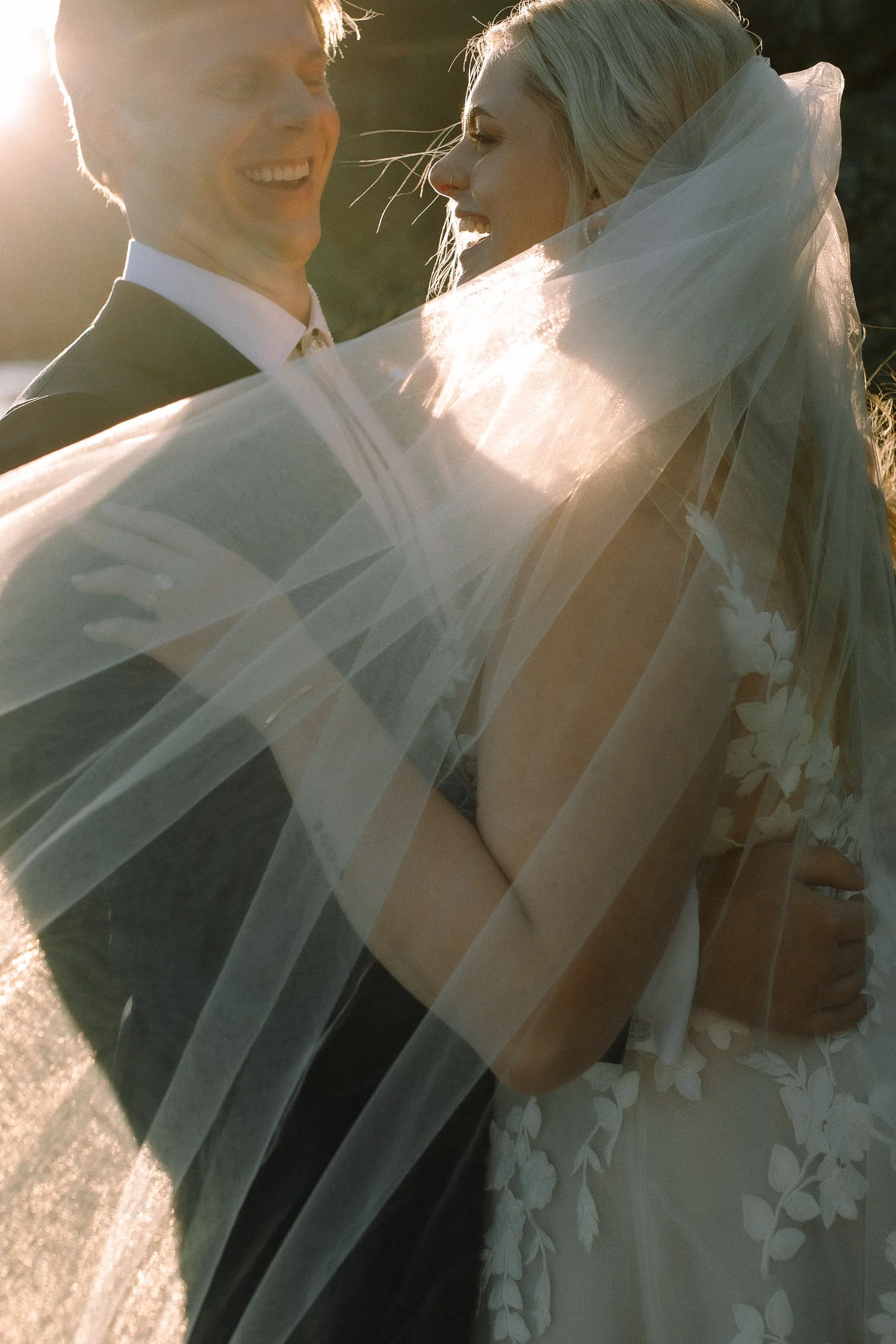 Bride and groom wrapped in veil during golden hour at College Cove