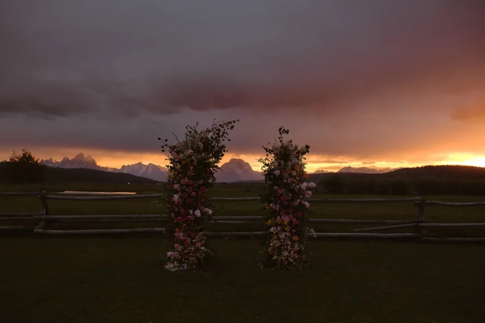 Floral ceremony pillars overlooking the Grand Tetons during a dramatic sunset wedding ceremony