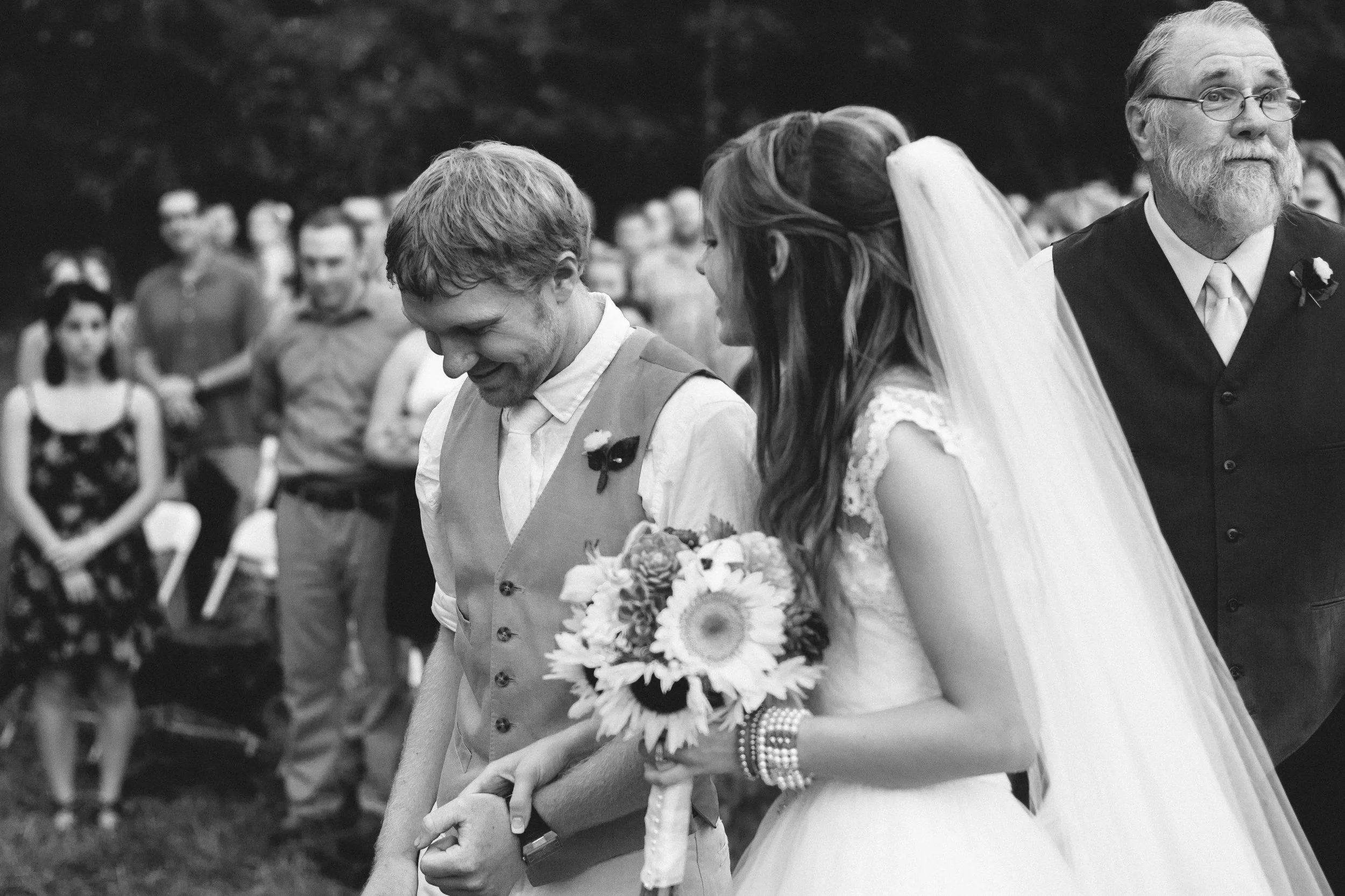 Meaningful wedding photo showing bride and groom walking together while father wipes tears during ceremony