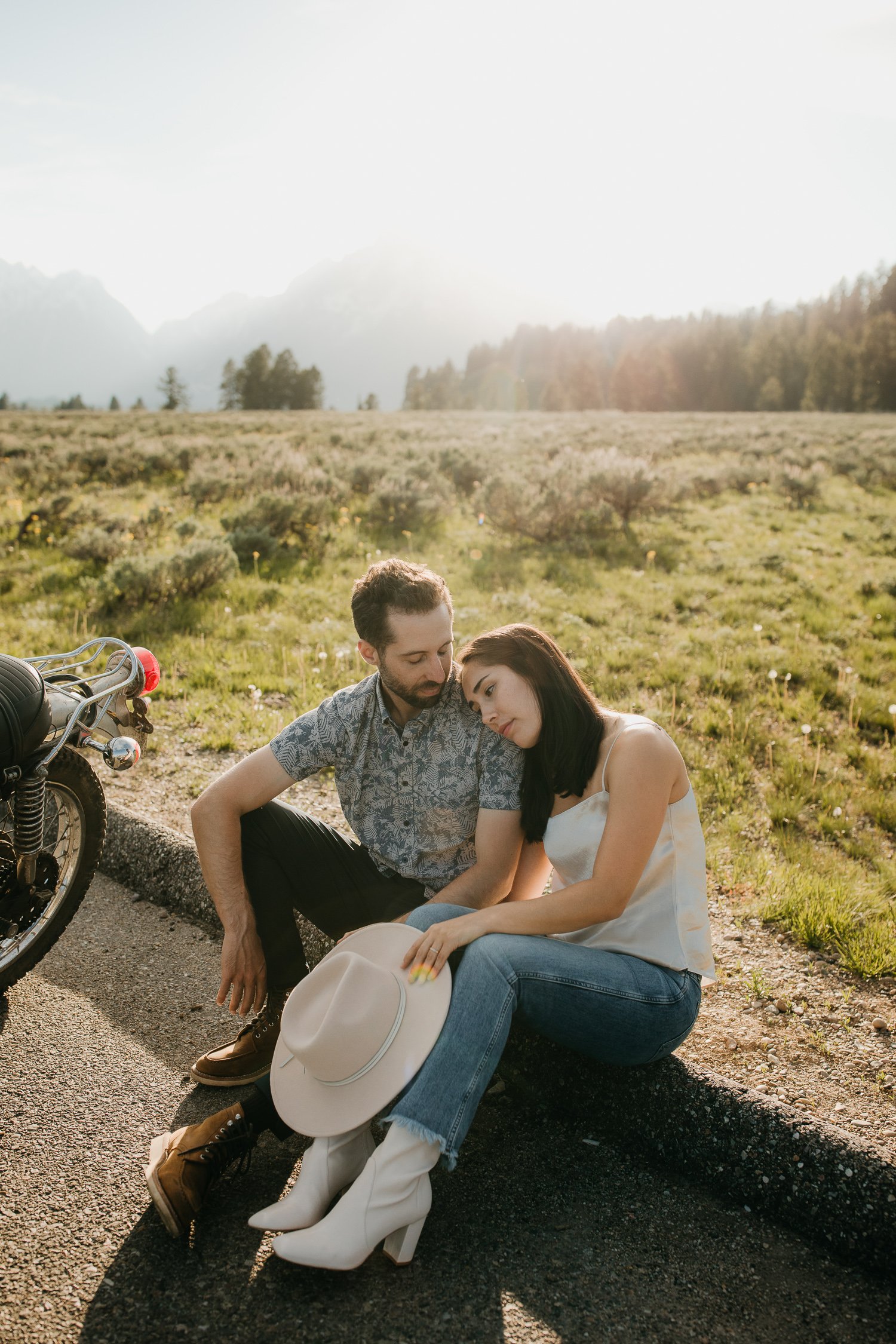 Couple sitting on the roadside beside a motorcycle during an engagement session