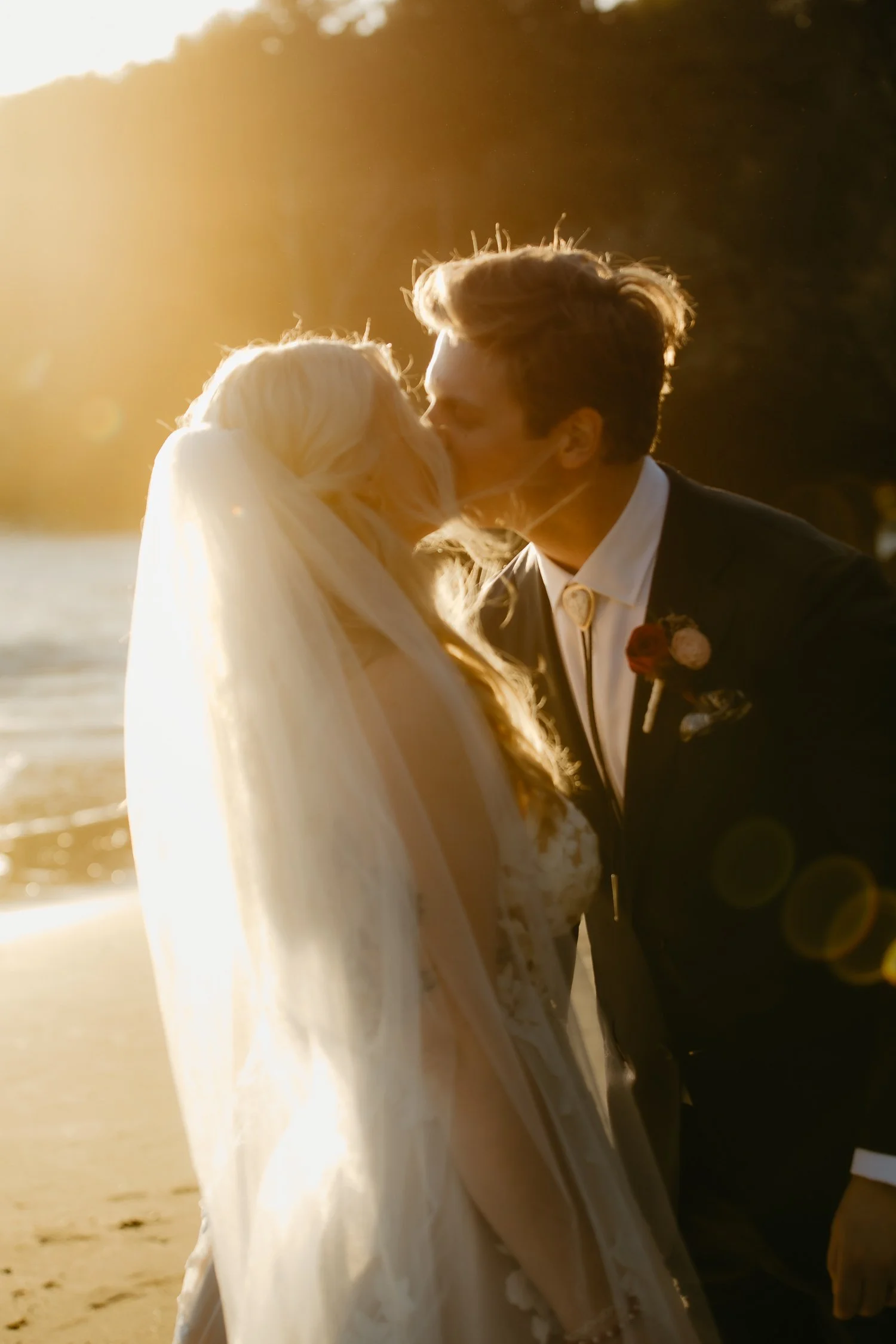Backlit sunset kiss between bride and groom at College Cove