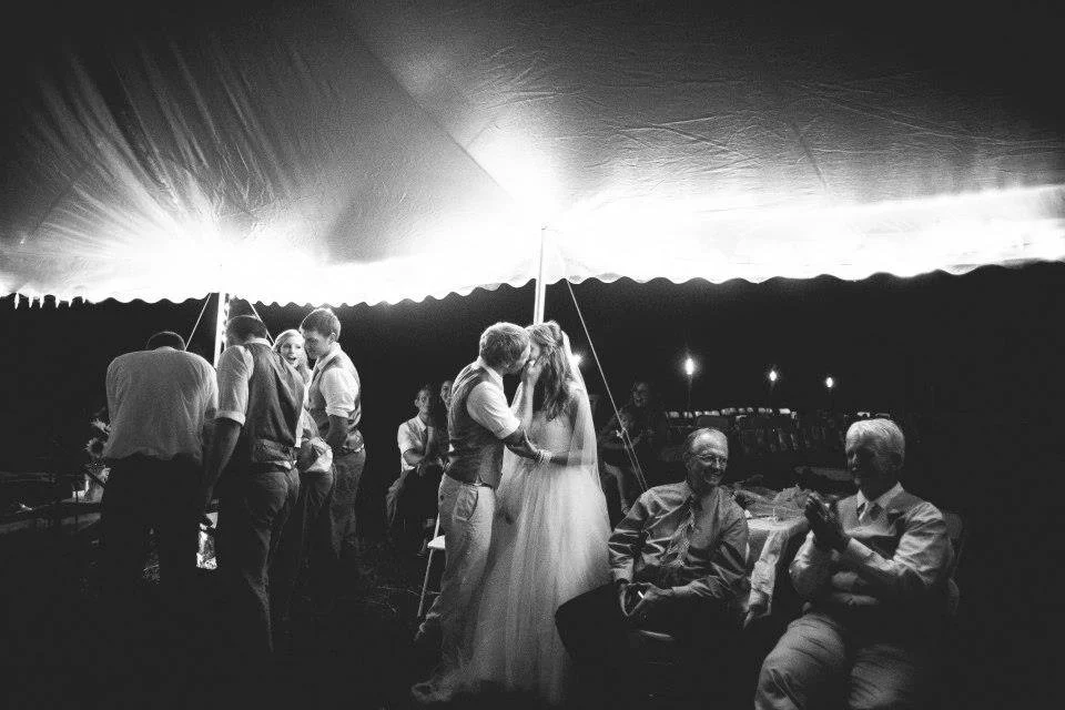 Candid wedding reception photo of couple kissing in tent, real documentary wedding moment