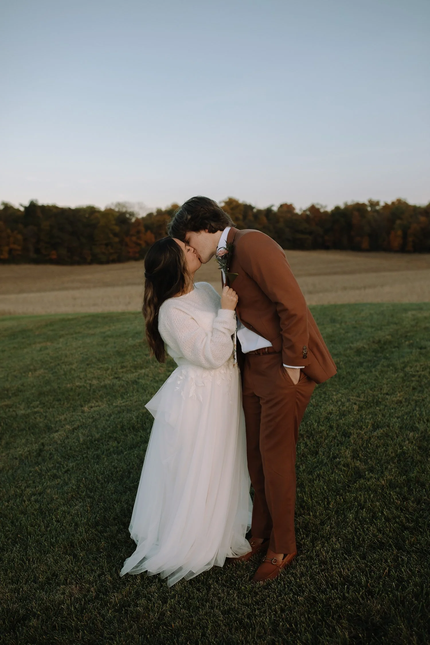 Bride and groom kissing during sunset wedding portraits in an open field at Ivory Meadows in Dayton, Ohio, with warm autumn light.