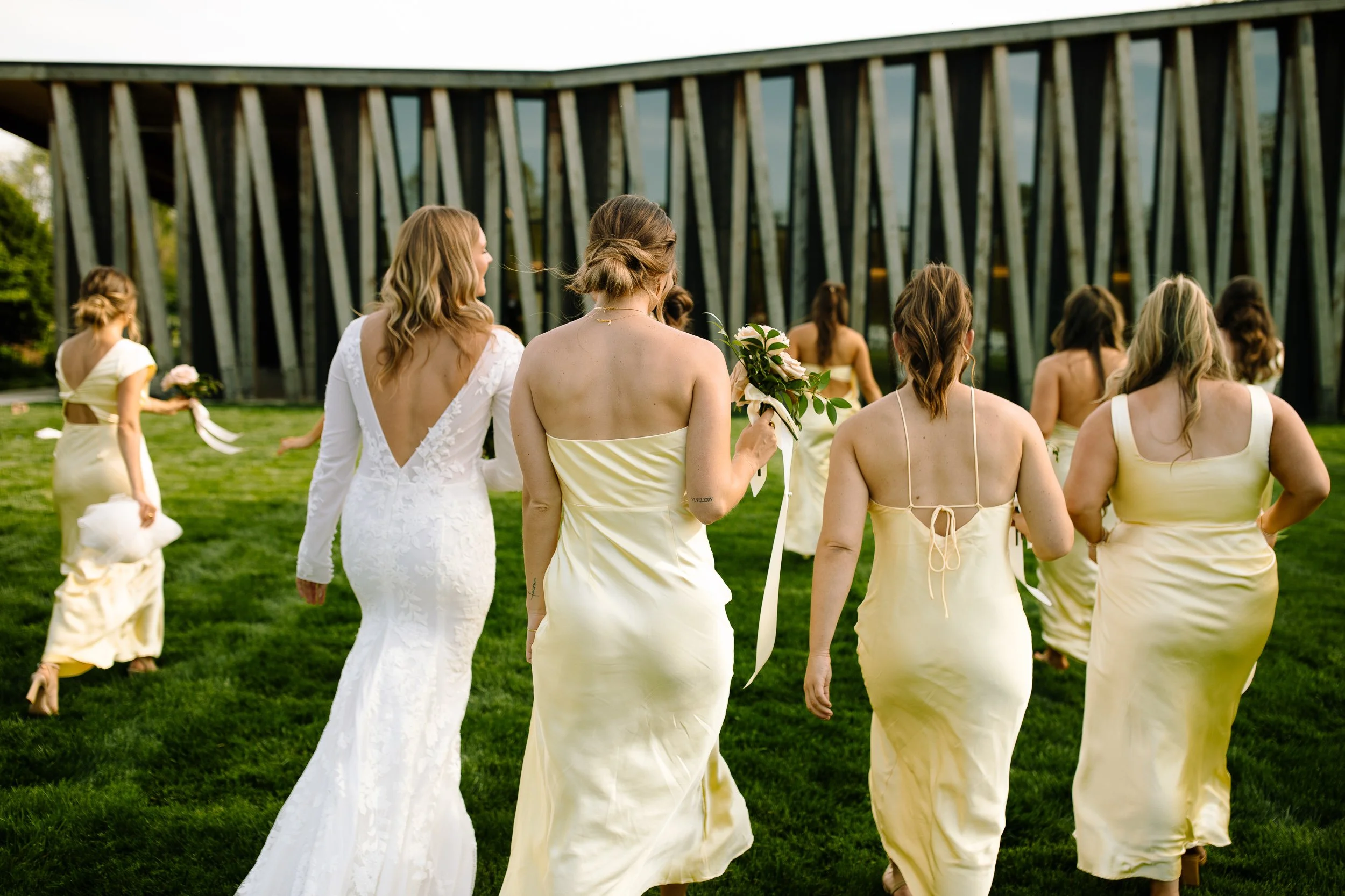 Bride walking with her bridesmaids in pale yellow dresses outside the Arboretum building at Jorgensen Farm The Gardens.
