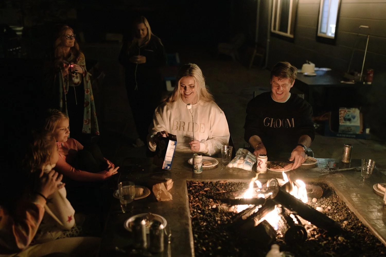 Couple and friends gathered around a fire pit making s’mores after their wedding