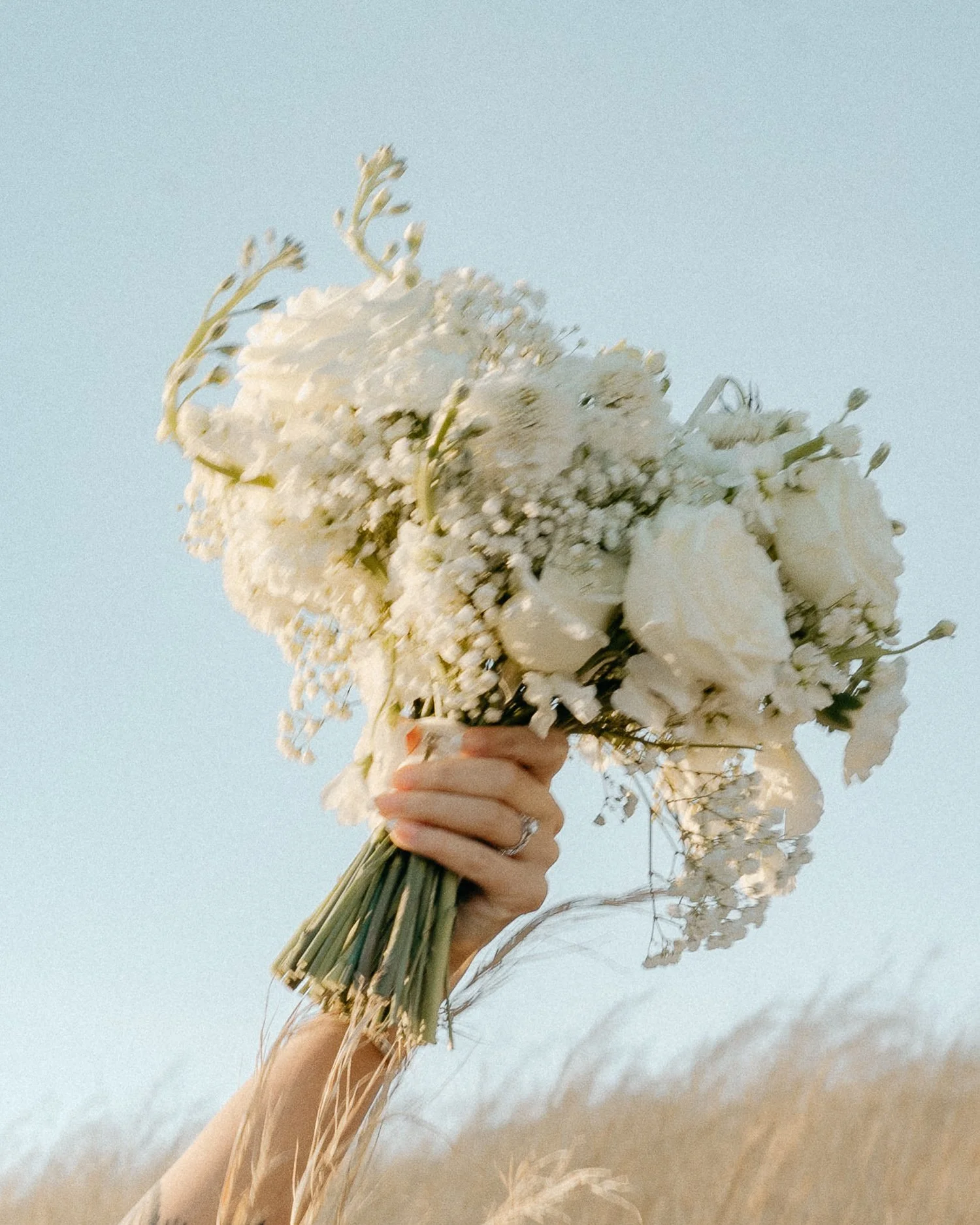 Bride holding white bouquet in soft natural light during wedding morning preparations