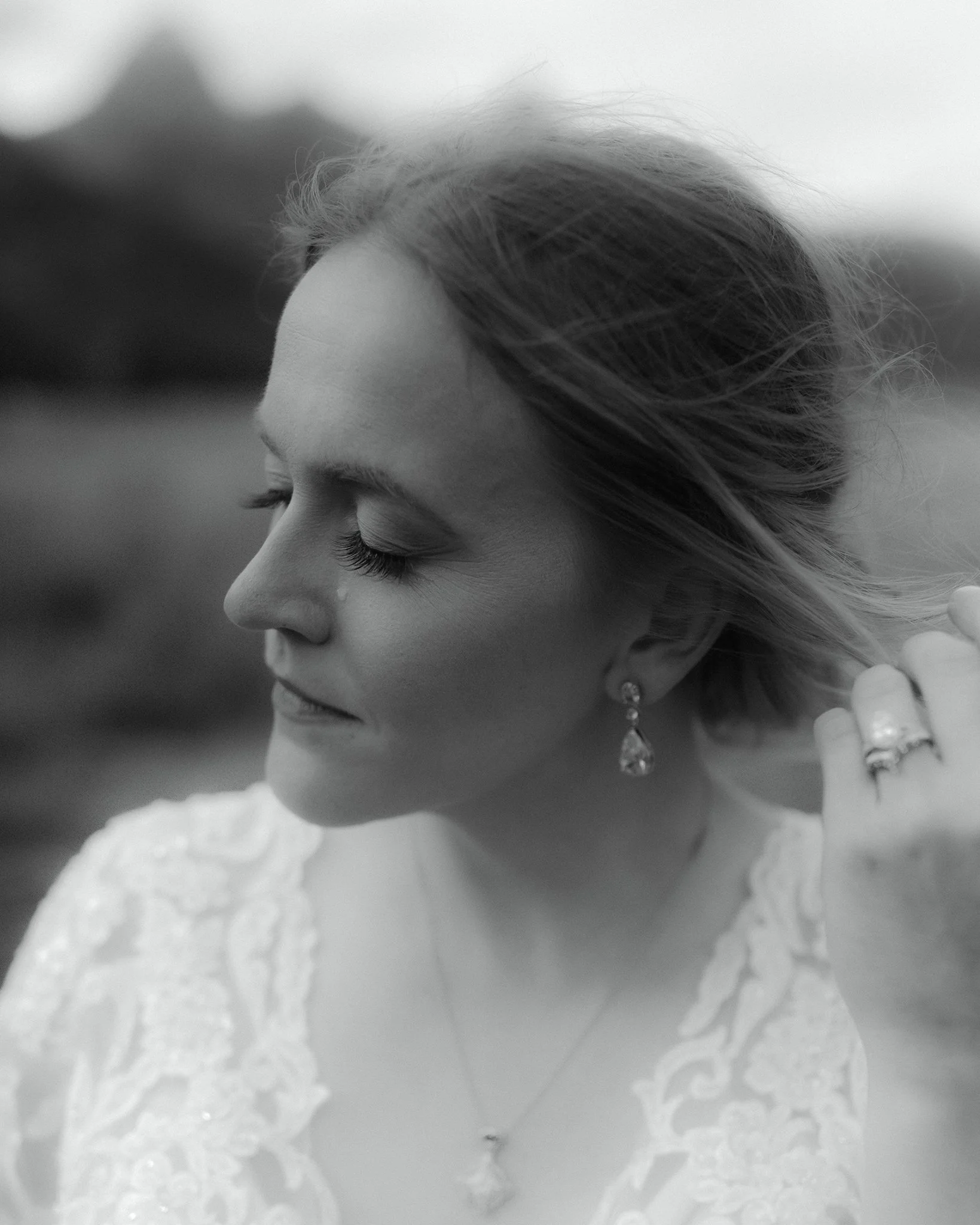 Close up black and white portrait of bride adjusting her hair in soft natural light before the ceremony.