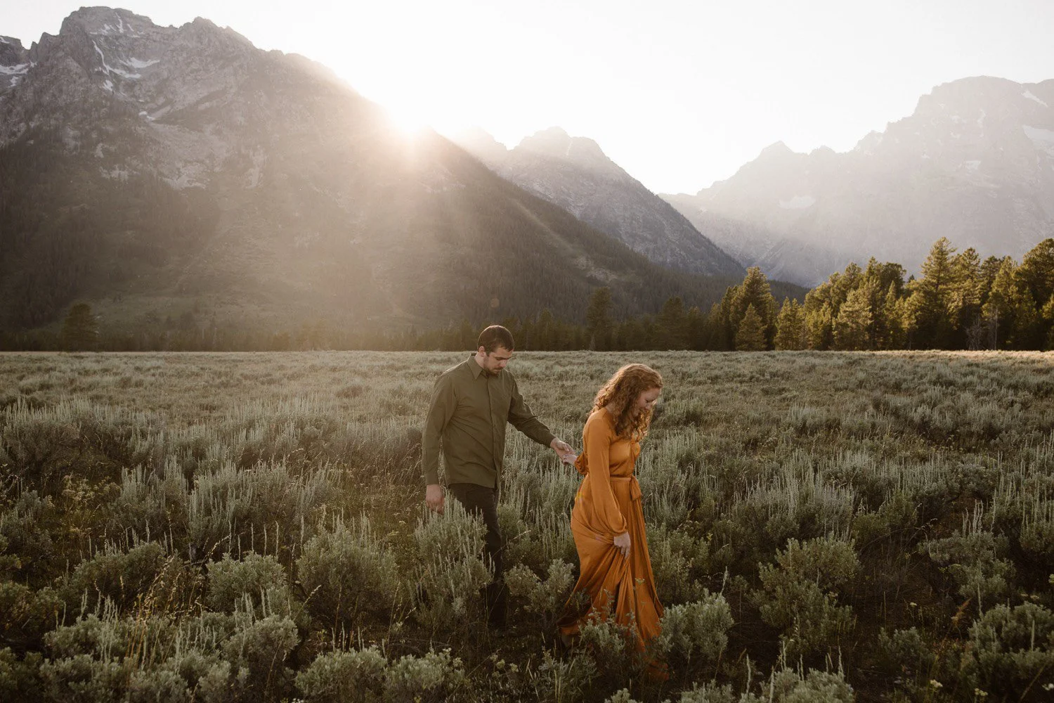 Couple walking together during golden hour with soft light and the Grand Teton mountains behind them.