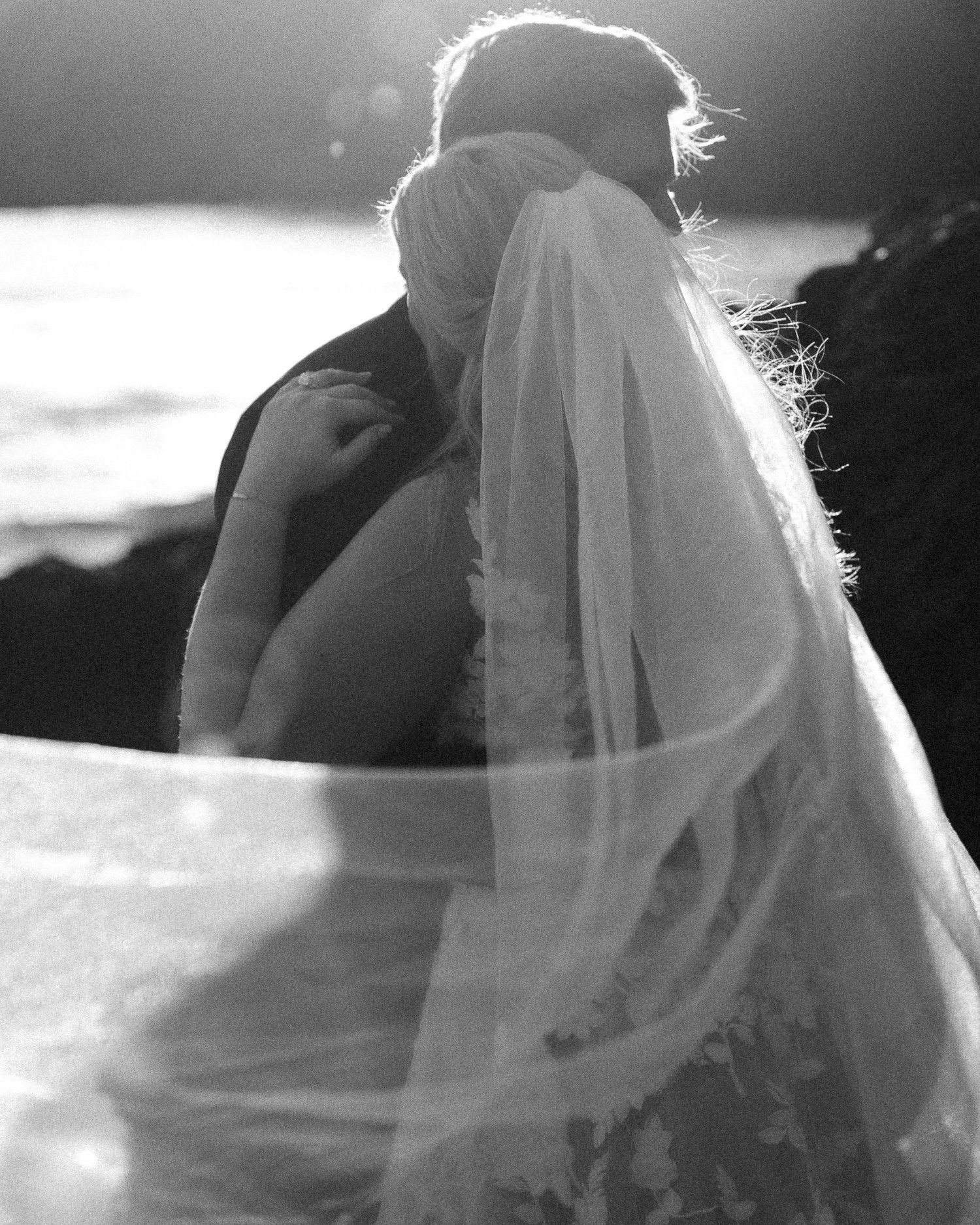 Black and white portrait of bride and groom embracing on the beach