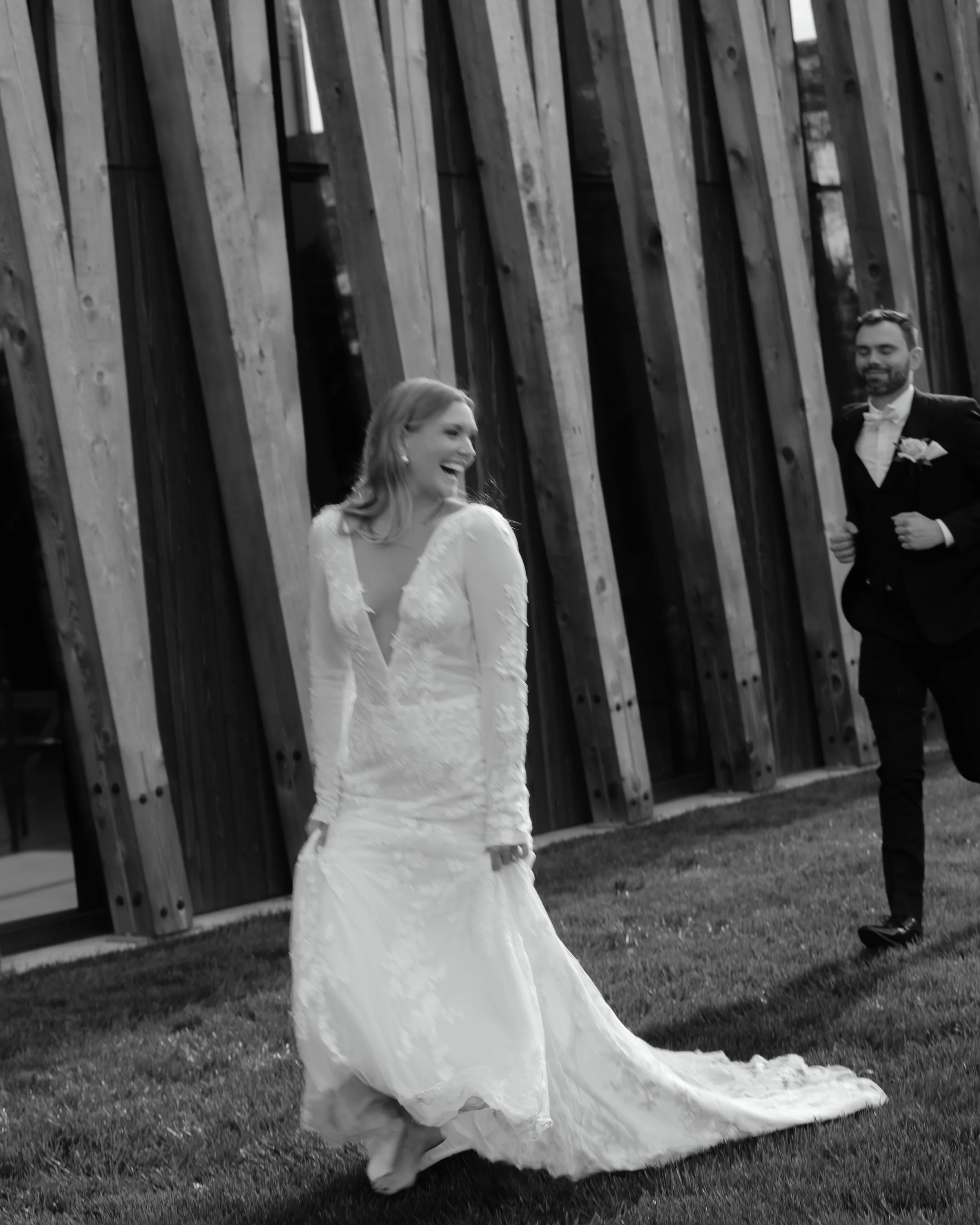Black and white portrait of the bride and groom laughing outside the Arboretum building at Jorgensen Farm.