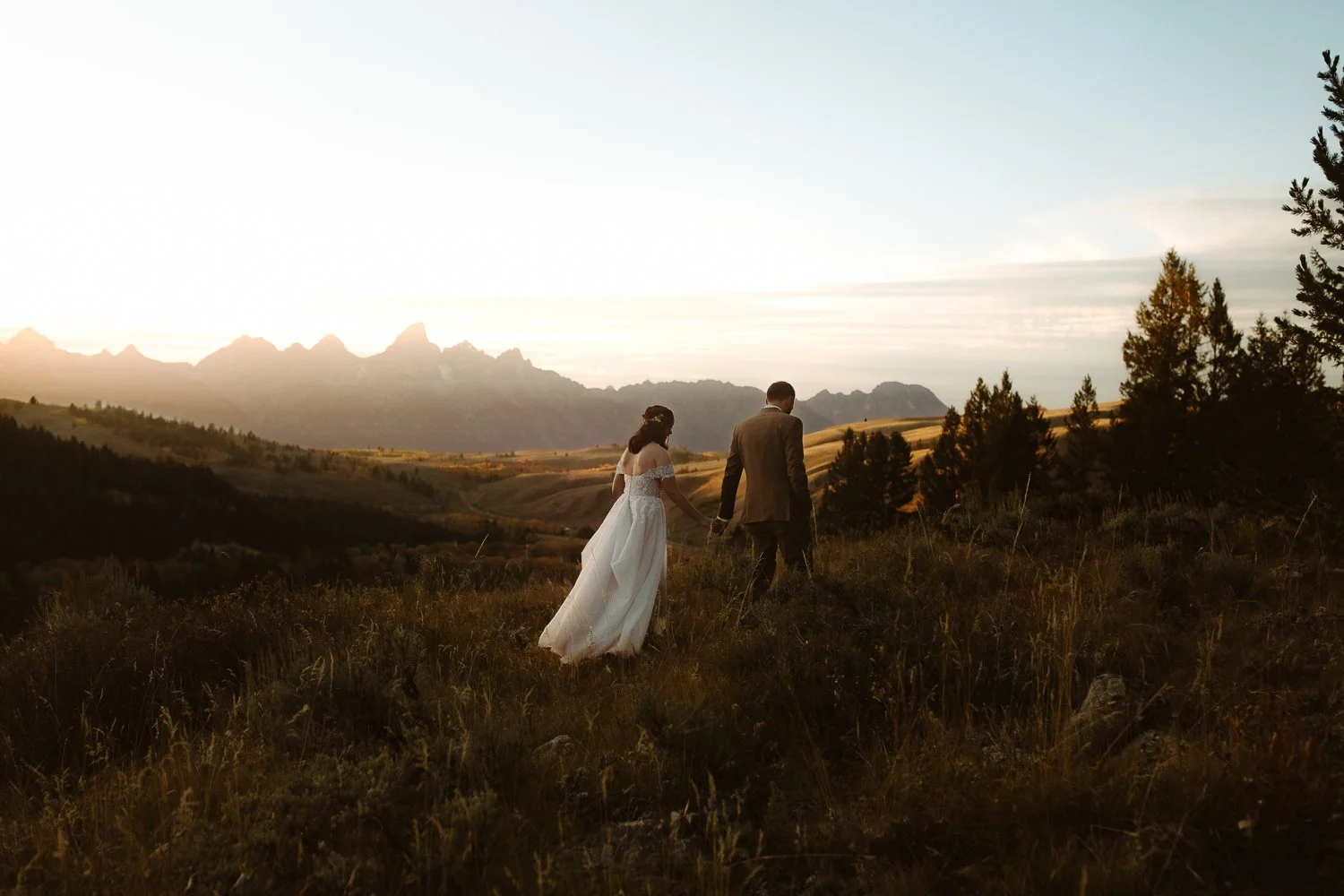 Couple walking together during a sunset elopement with the Grand Teton mountain range in the distance.
