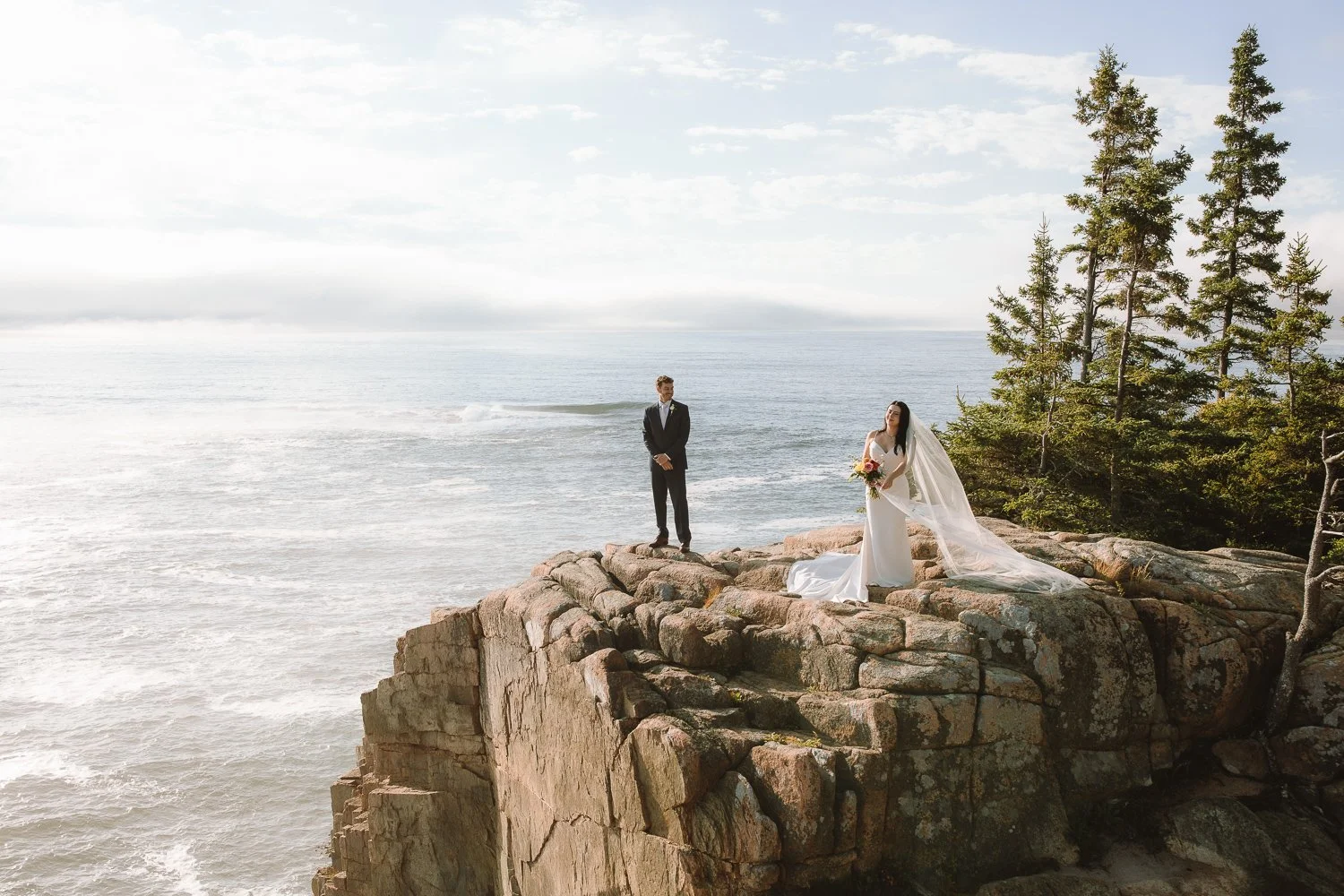 Couple standing on a rocky cliff edge overlooking the ocean during an Acadia National Park elopement