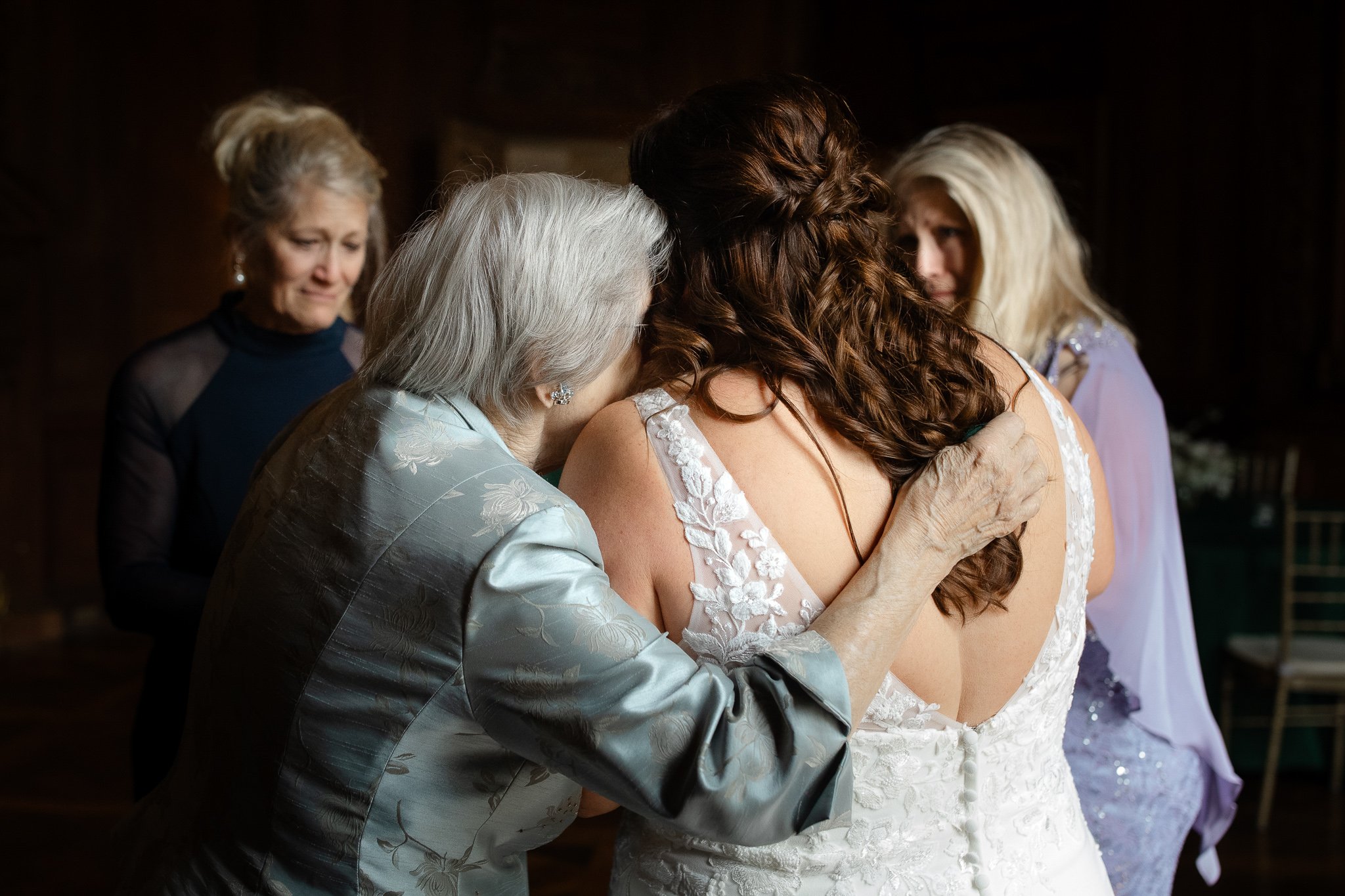 Grandmother embracing bride from behind during emotional wedding moment