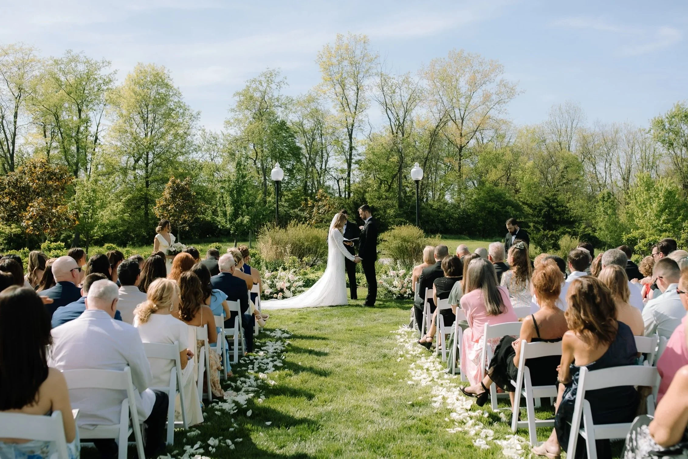 Outdoor wedding ceremony on the lawn at Jorgensen Farm The Gardens in Columbus, Ohio, with guests seated in white chairs.