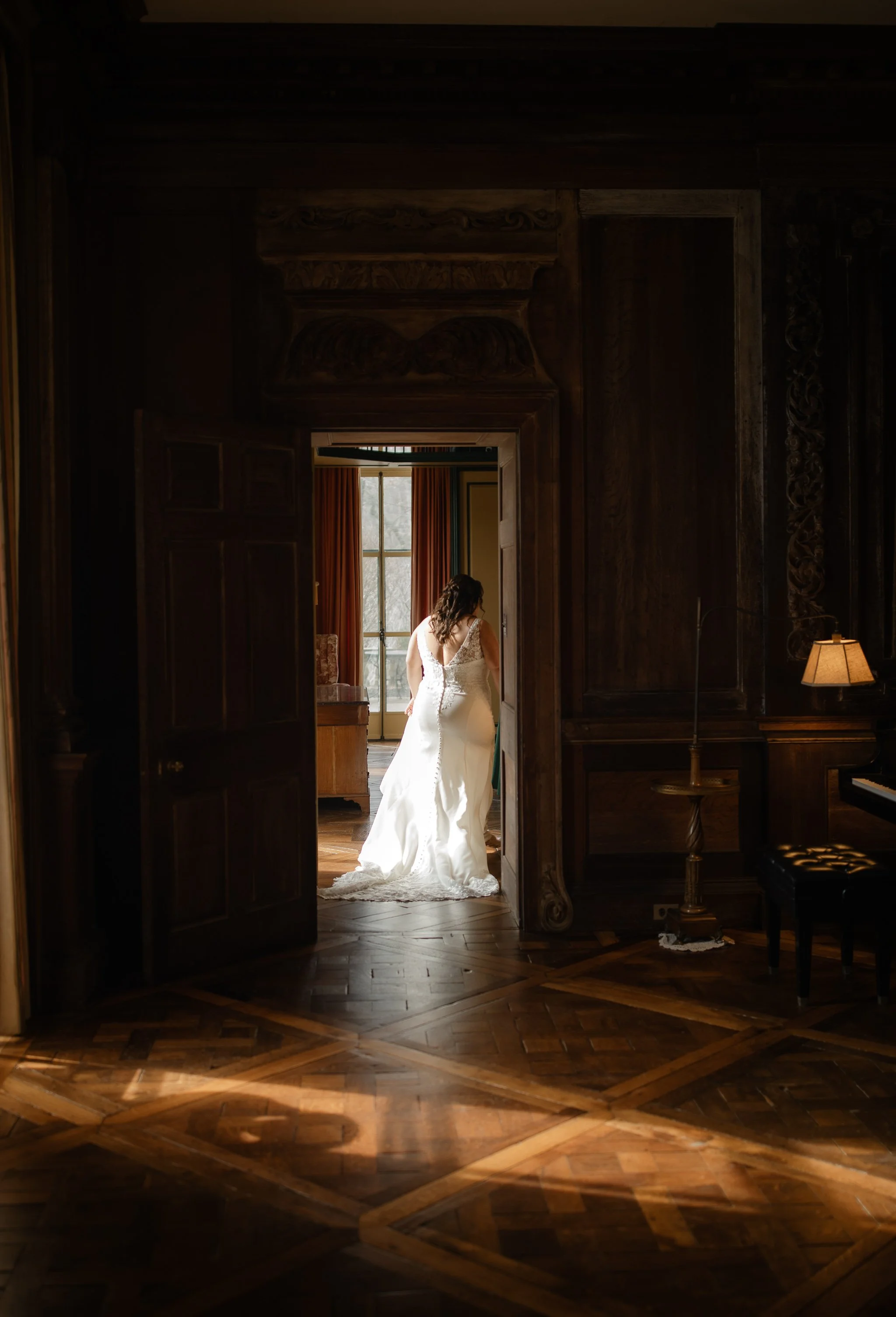 Bride walking through doorway inside Peterloon Estate with warm light and wood-paneled interior