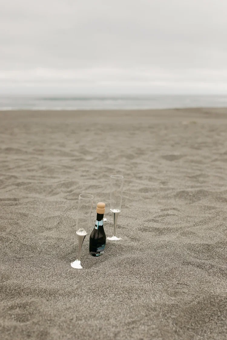 Champagne bottle and glasses set in the sand during a beach elopement
