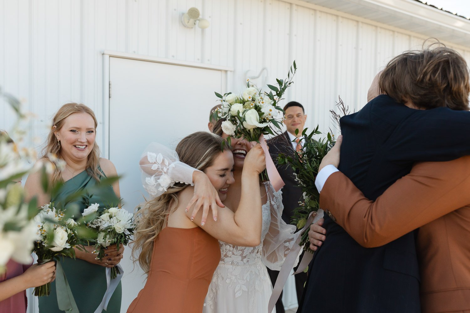 Joyful post-recessional moment as the bride hugs a bridesmaid holding her bouquet at Ivory Meadows in Dayton, Ohio.