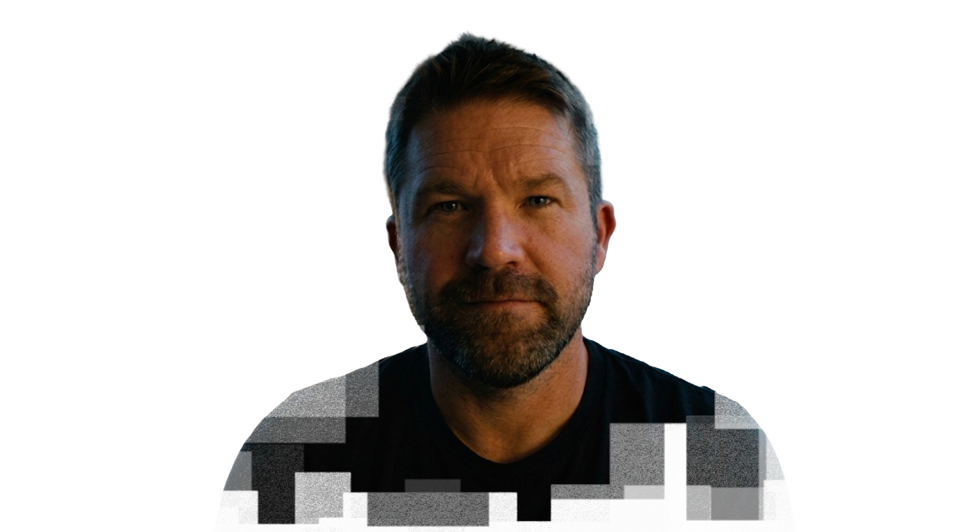 Portrait of a man with short brown hair, a beard, and a serious expression, wearing a black shirt, against a black background with colorful digital artifacts on the right side.