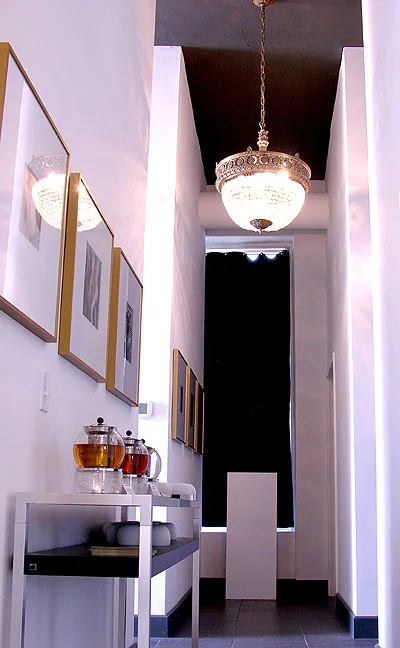 A highly decorative bronze and crystal chandelier illuminates the hallway, its unique beauty is emphasized by the dark brown ceiling.