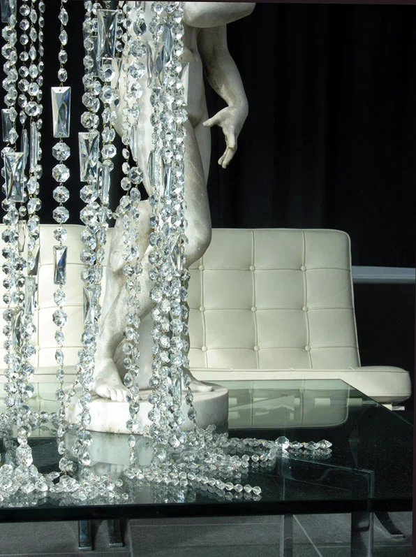 When attention was turned to the design of the front of the building, Denny sought a lighting fixture that would work with the narrow space that was surrounded by windows that faces busy Central Avenue. Listening to Denny’s needs and ideas, a custom built light fixture was designed by Architectural Antiques which resulted in a 14 foot, 3 tiered crystal chandelier which takes advantage of the visibility of the salon and fills the space with ropes of hand strung crystals. The crystals pool onto the top of a glass table which shares its space with an original 1920's marble statue, also supplied by Architectural Antiques. 