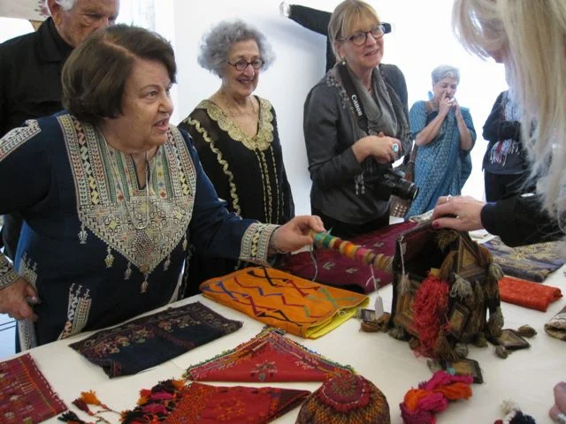Widad Kamar explains the use of the hanging basket for storing embroidery in progress, showing a wooden bobbin with unspun silk threads from inside the basket.