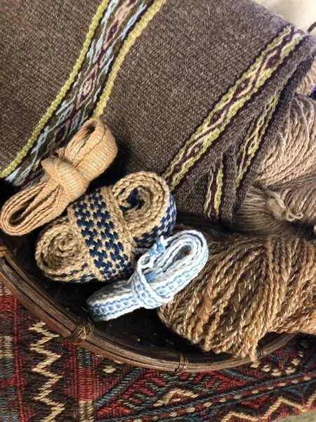 Handwoven warp-faced wool with pickup designs, Navajo churro is the main color, bundles of cotton handwoven tape, a few skeins of handspun wool yarn, in a basket on top of a Turkish handwoven salt bag.