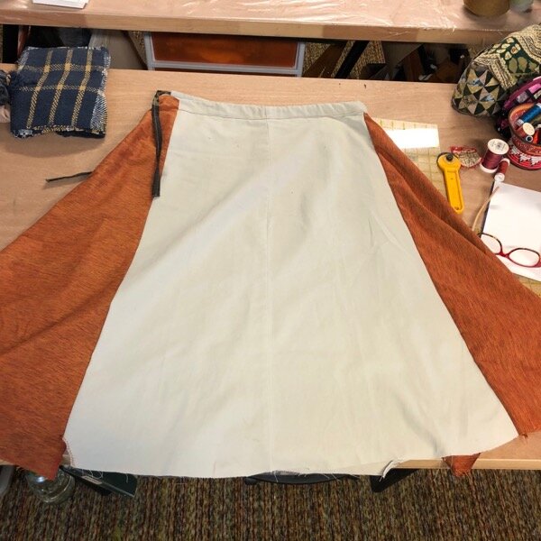 Inverted leg of khaki pants, spread flat and bordered by orange cotton blend - half the skirt in side view, with drawstring, before pockets.