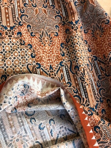 Print sarong, showing underside. Intricate batik-style patterns in shades of pink/brown and indigo blue, with black and white highlights.