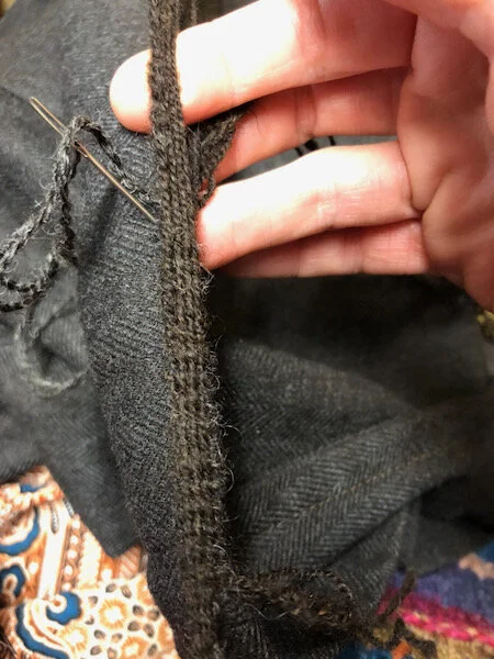 Card weaving in progress. The tricky part was figuring out how to hold it, to keep the shed open, tension on, stitch the weft through, etc. Hand had to learn the best method to avoid hours of awkwardness. The point nearest me is pinned to my belt, and the far end attached to a clamp on the table.