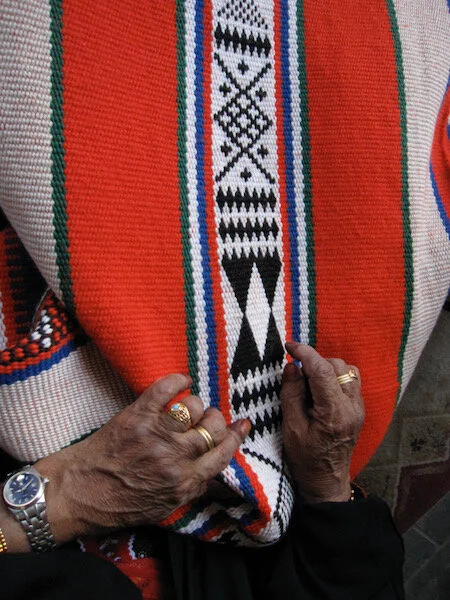 Um Hamad points out the patterns in a weaving. The rows of black diamonds seem to make boundary lines between designs, and would also serve to catch any long floats.