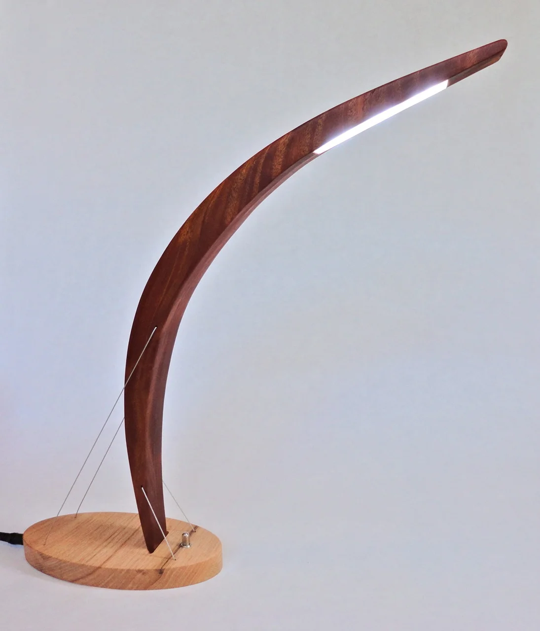 Peering lamp by Robby Cuthbert. A carefully engineered modern Led lamp. The sculptural piece features a mahogany curve carefully balanced atop an oak base and held in place by steel cables under tension.