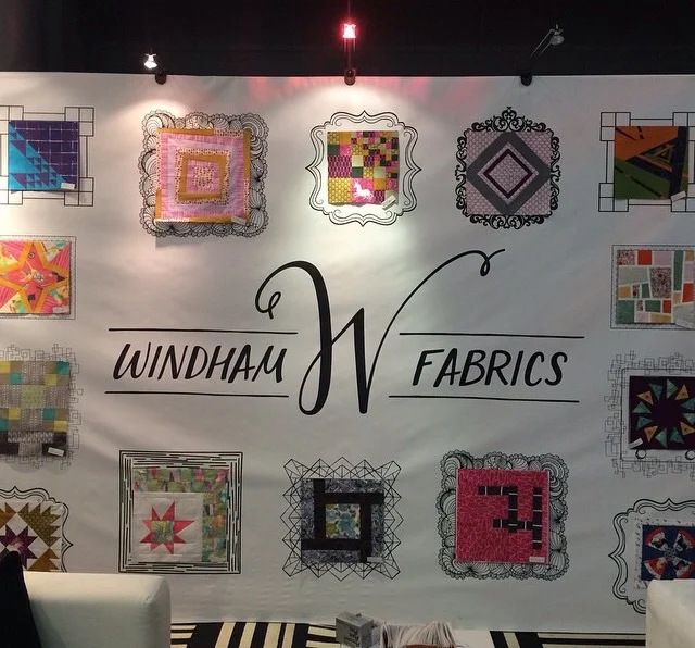 A close up of the booth wall featuring the redesigned logo and my doodle frame (right above the word Windham) Photo courtesy of @windhamfabrics on Instagram.